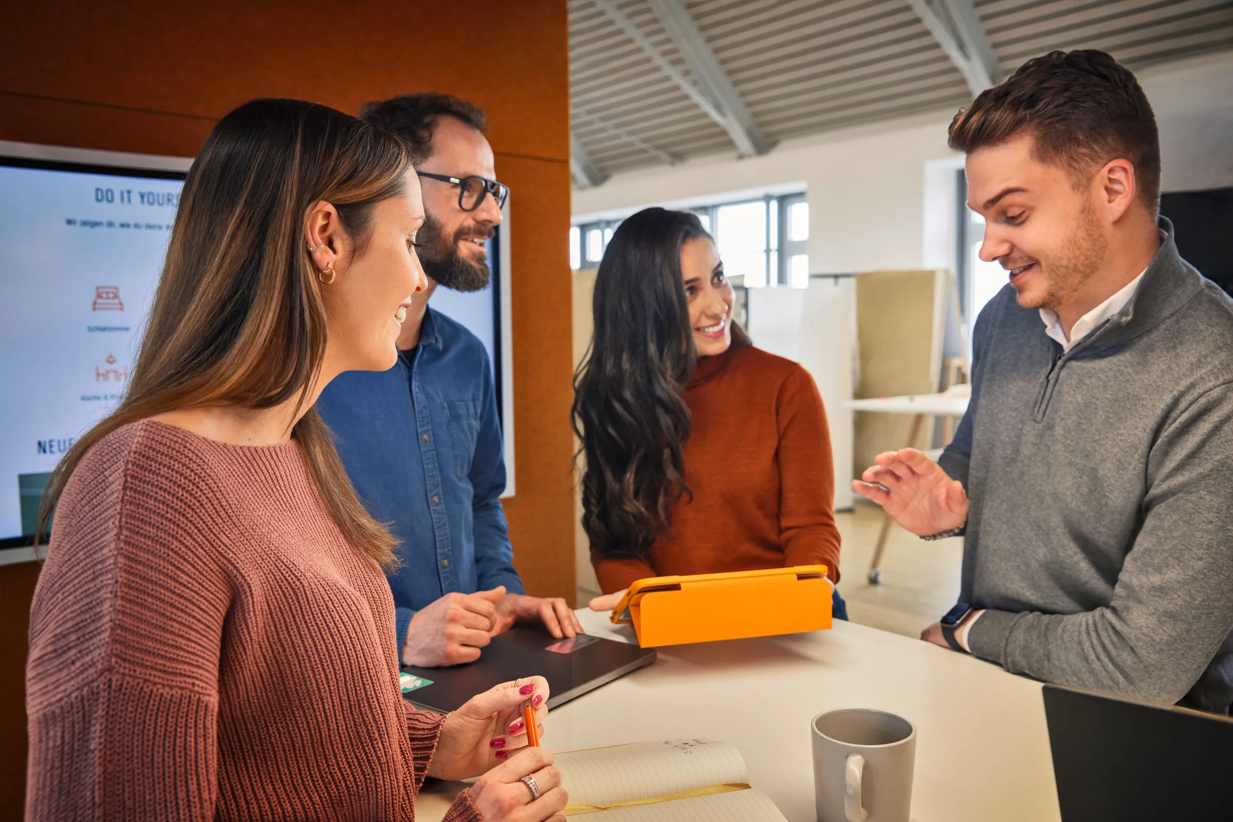 Vier junge Kollegen besprechen gemeinsam ein Projekt im modernen Büro bei OBI – Teamarbeit im Einzelhandel.
