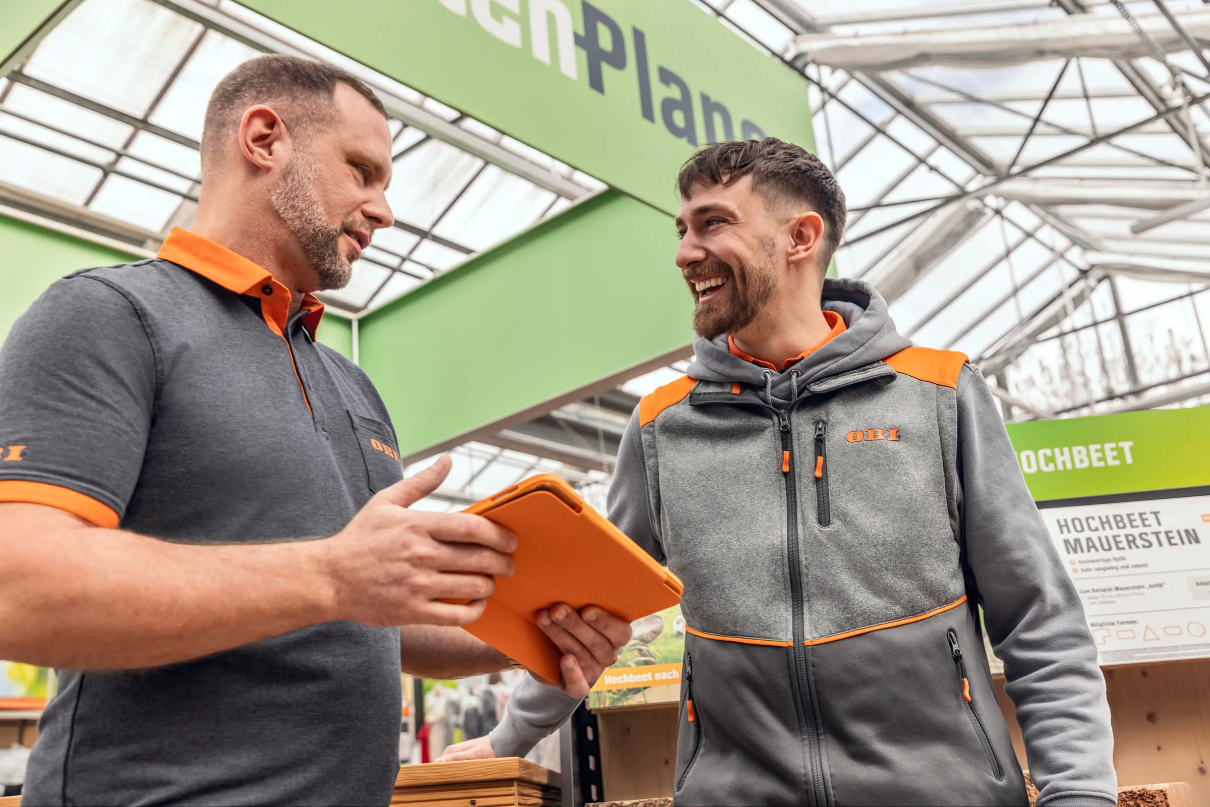 Zwei OBI-Mitarbeiter im Markt, die sich freundlich unterhalten und gemeinsam auf ein Tablet schauen.