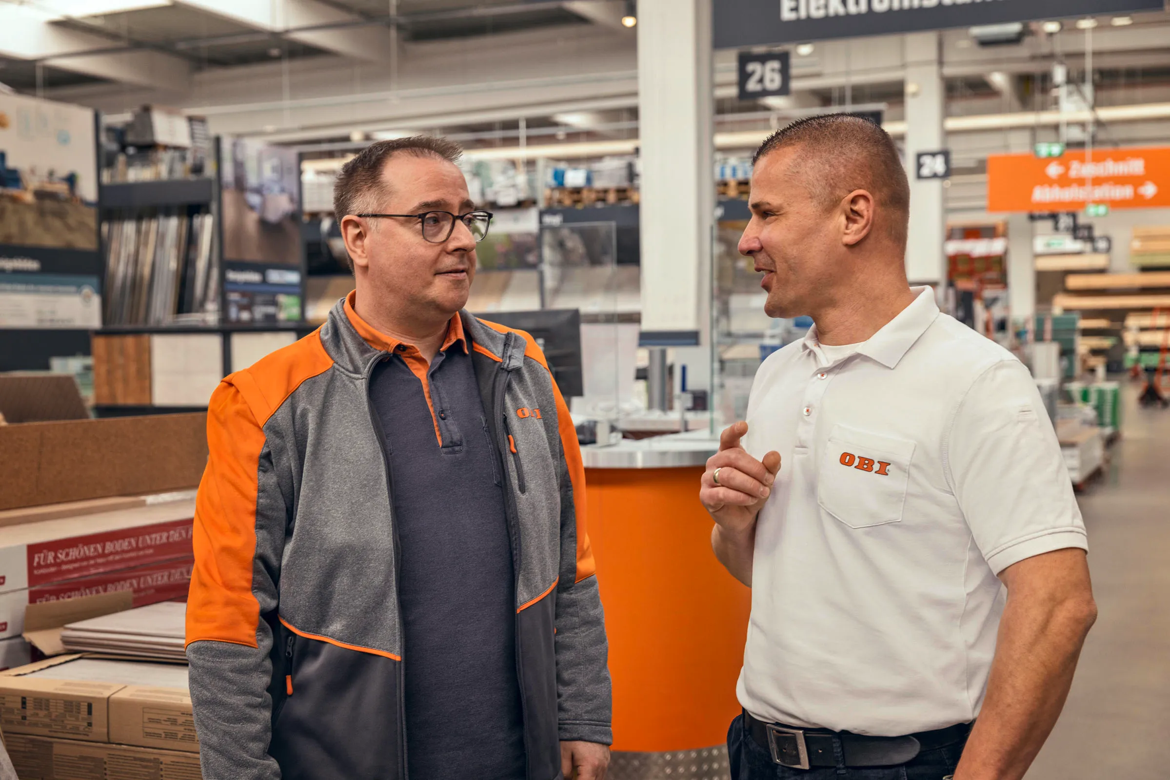 Zwei OBI-Mitarbeiter beraten Dich freundlich bei der Auswahl von Stoffmustern in einem modernen Baumarkt.