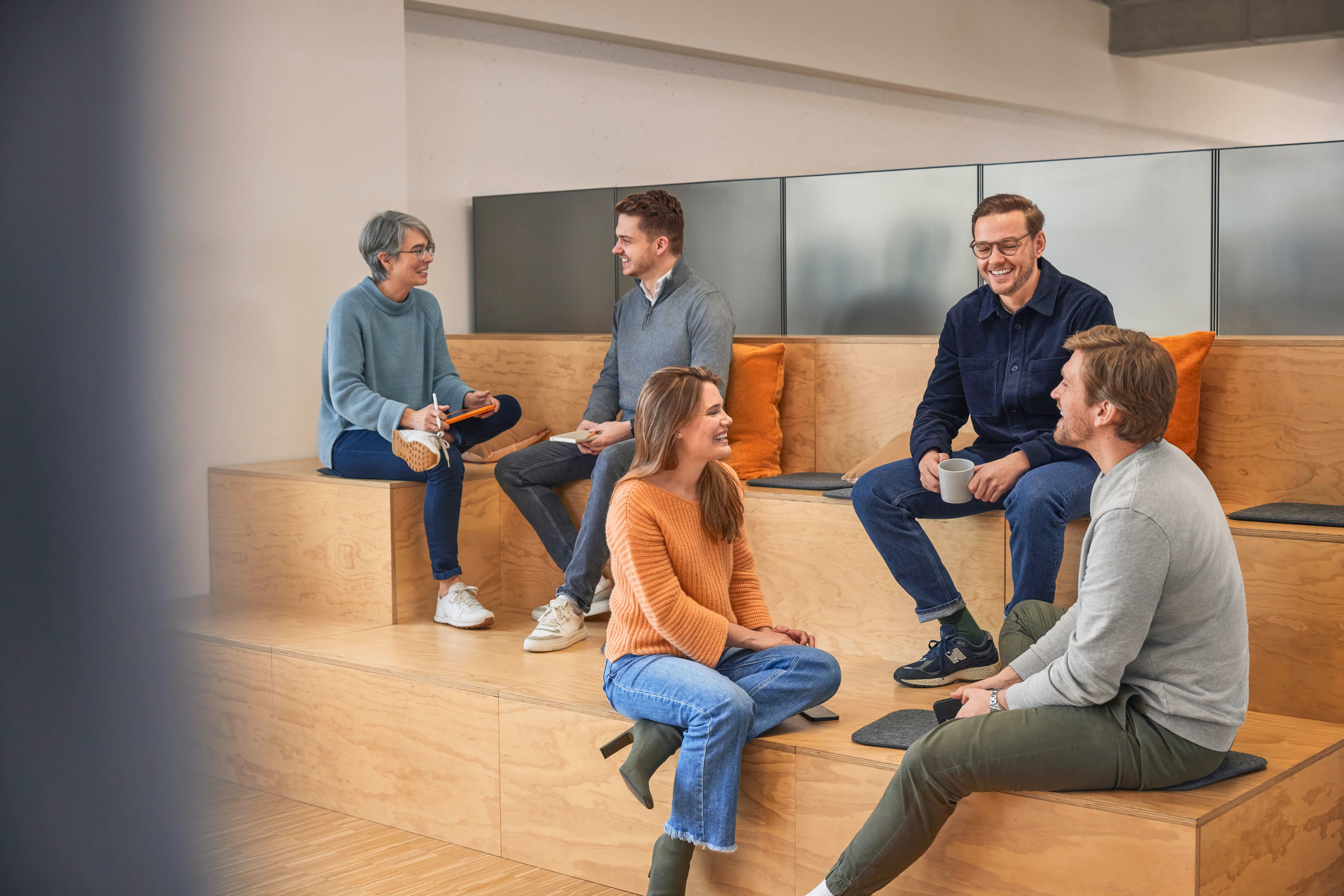 Fünf OBI Mitarbeitende sitzen entspannt zusammen und unterhalten sich in moderner Arbeitsumgebung.