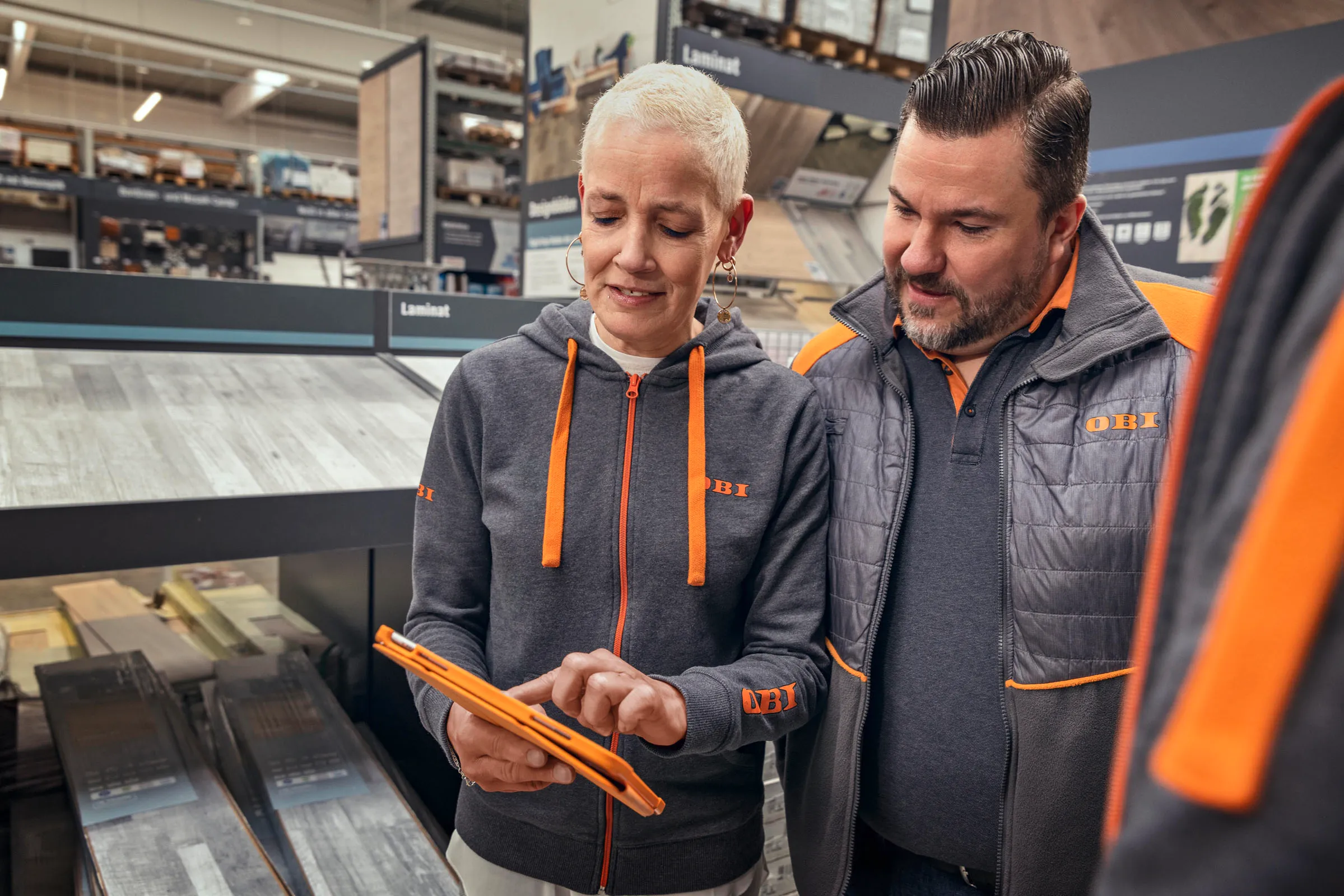 Zwei OBI-Mitarbeitende besprechen gemeinsam etwas auf einem Tablet in der Laminat-Abteilung.