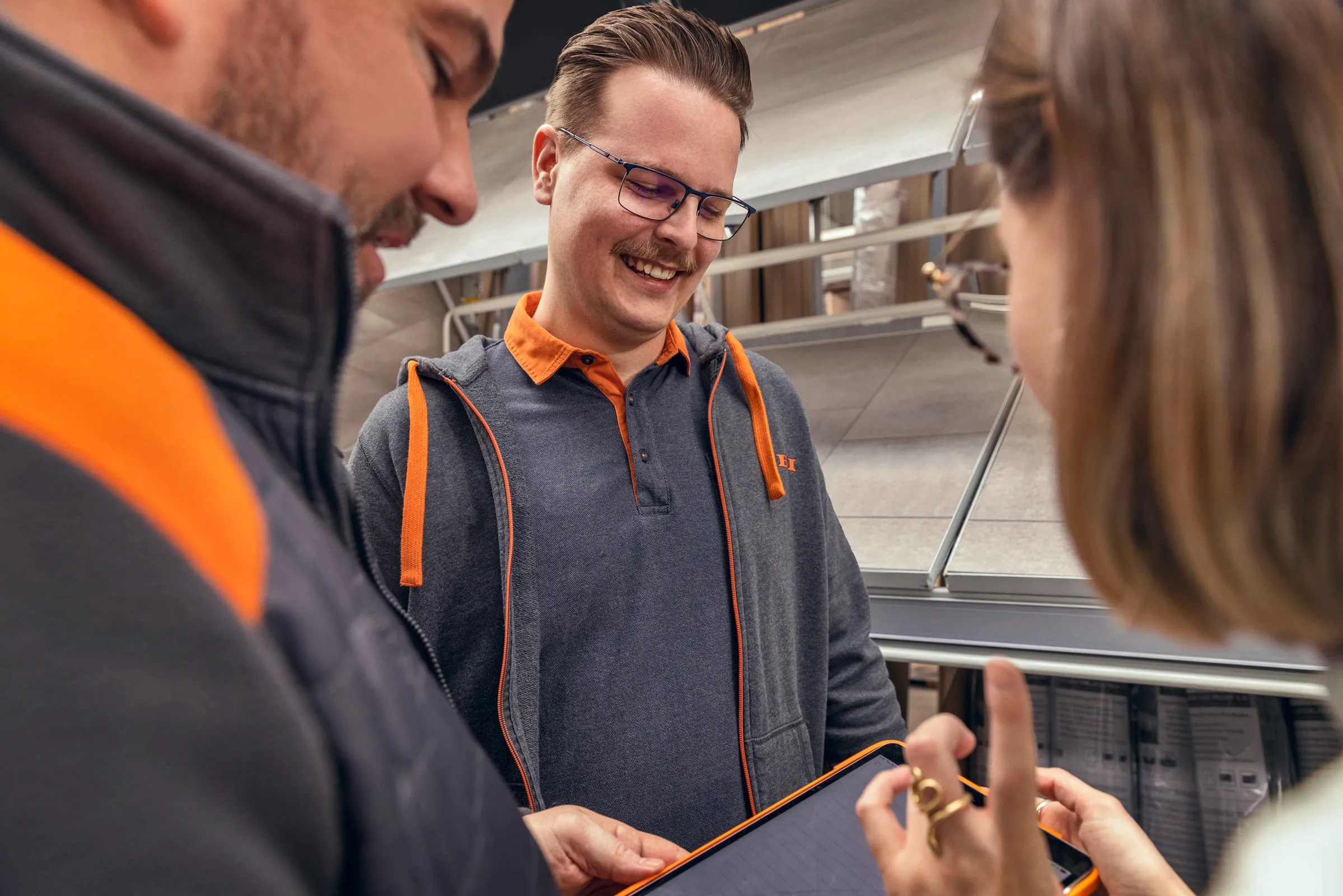 Drei OBI Mitarbeitende im Gespräch, eine Person zeigt etwas auf einem Tablet – Teamarbeit im Einzelhandel.