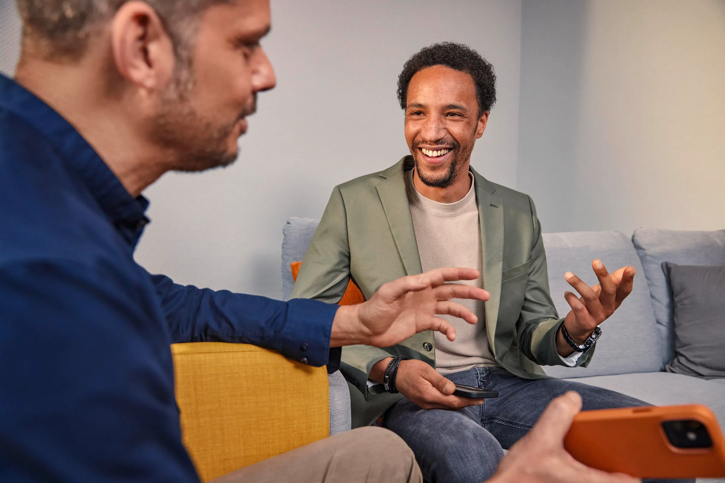 Zwei Kollegen im Gespräch auf dem Sofa, einer lacht – Teamarbeit und offene Kommunikation bei OBI.
