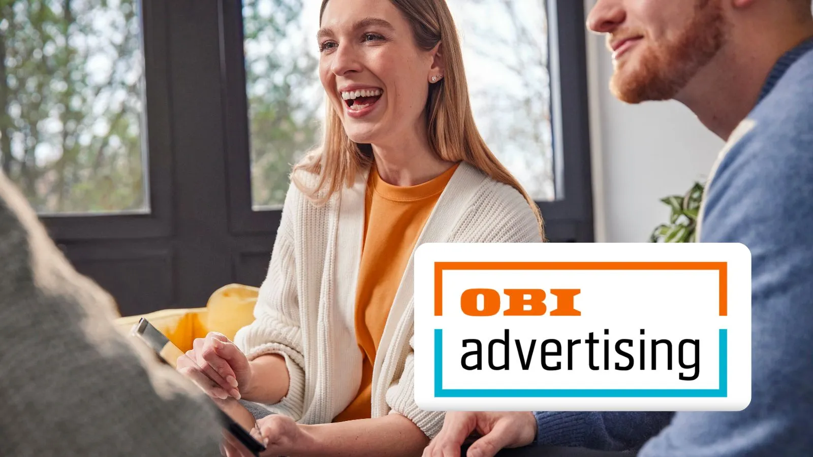 Drei junge Menschen lachen und besprechen gemeinsam Ideen in einem modernen Büro, OBI advertising Logo im Vordergrund.