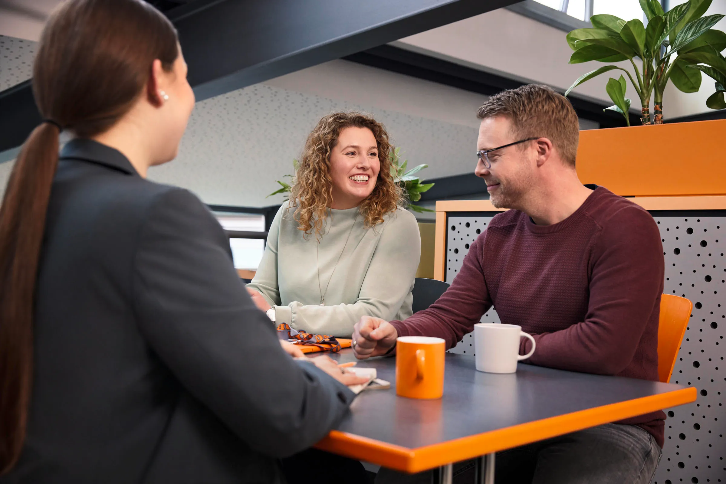 Drei Kolleg:innen unterhalten sich freundlich an einem Tisch im modernen Büro von OBI Group Holding.