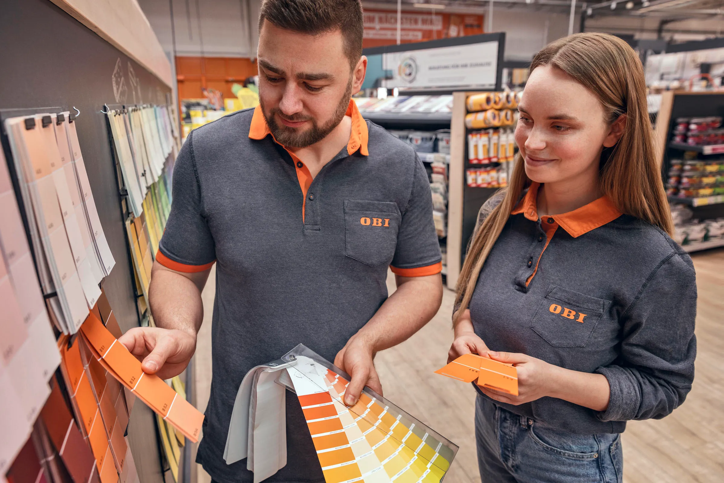 Zwei OBI Mitarbeitende beraten sich im Baumarkt über Farbmuster für die Kundenberatung.
