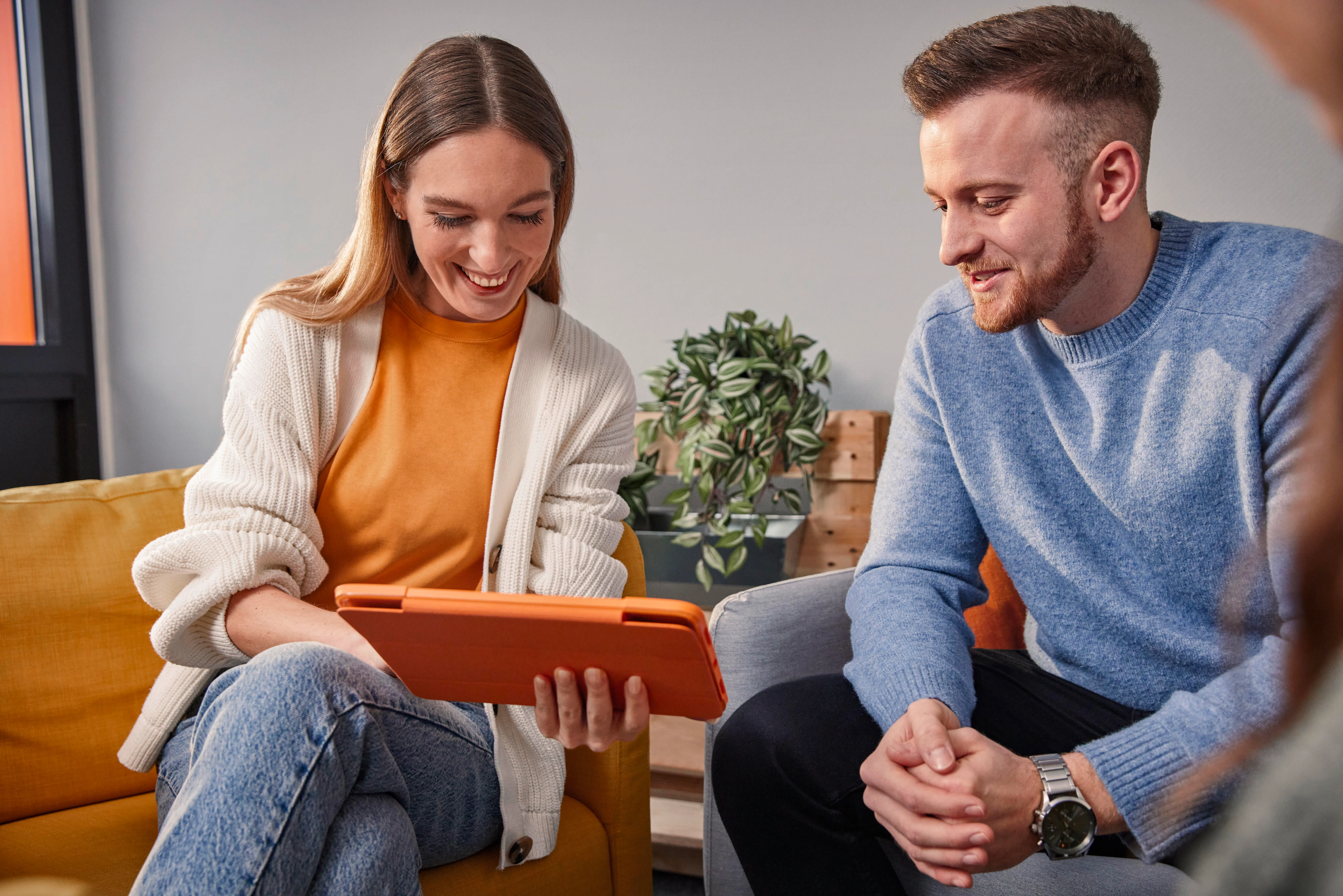 Zwei junge Kolleg:innen bei OBI schauen gemeinsam lachend auf ein Tablet und arbeiten im modernen Büro zusammen.
