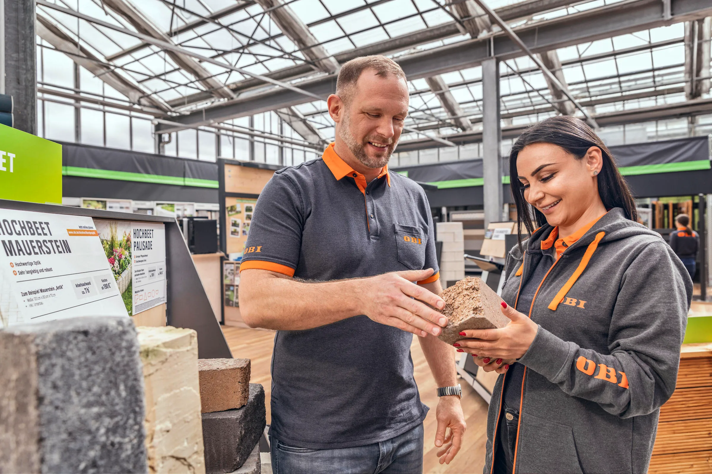 Drei OBI-Mitarbeitende unterhalten sich freundlich im Holzlager eines Baumarkts.