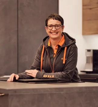 Eine lächelnde Mitarbeiterin von OBI AT GmbH steht in einer modernen Küche und trägt ein OBI-Logo auf ihrer Kleidung.