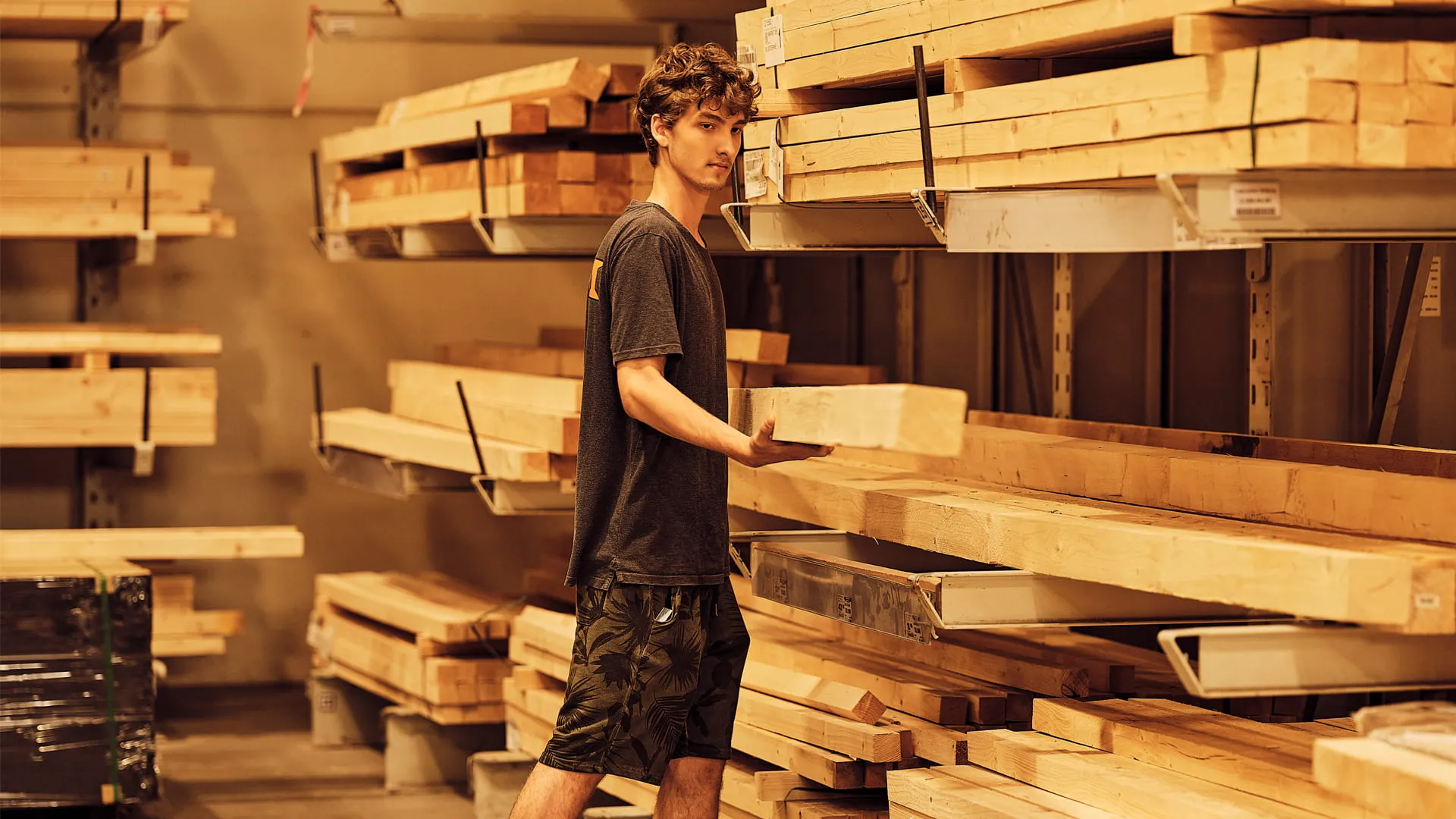 Ein Mitarbeiter nimmt ein Holzbrett aus einem Regal in einem Baumarkt.