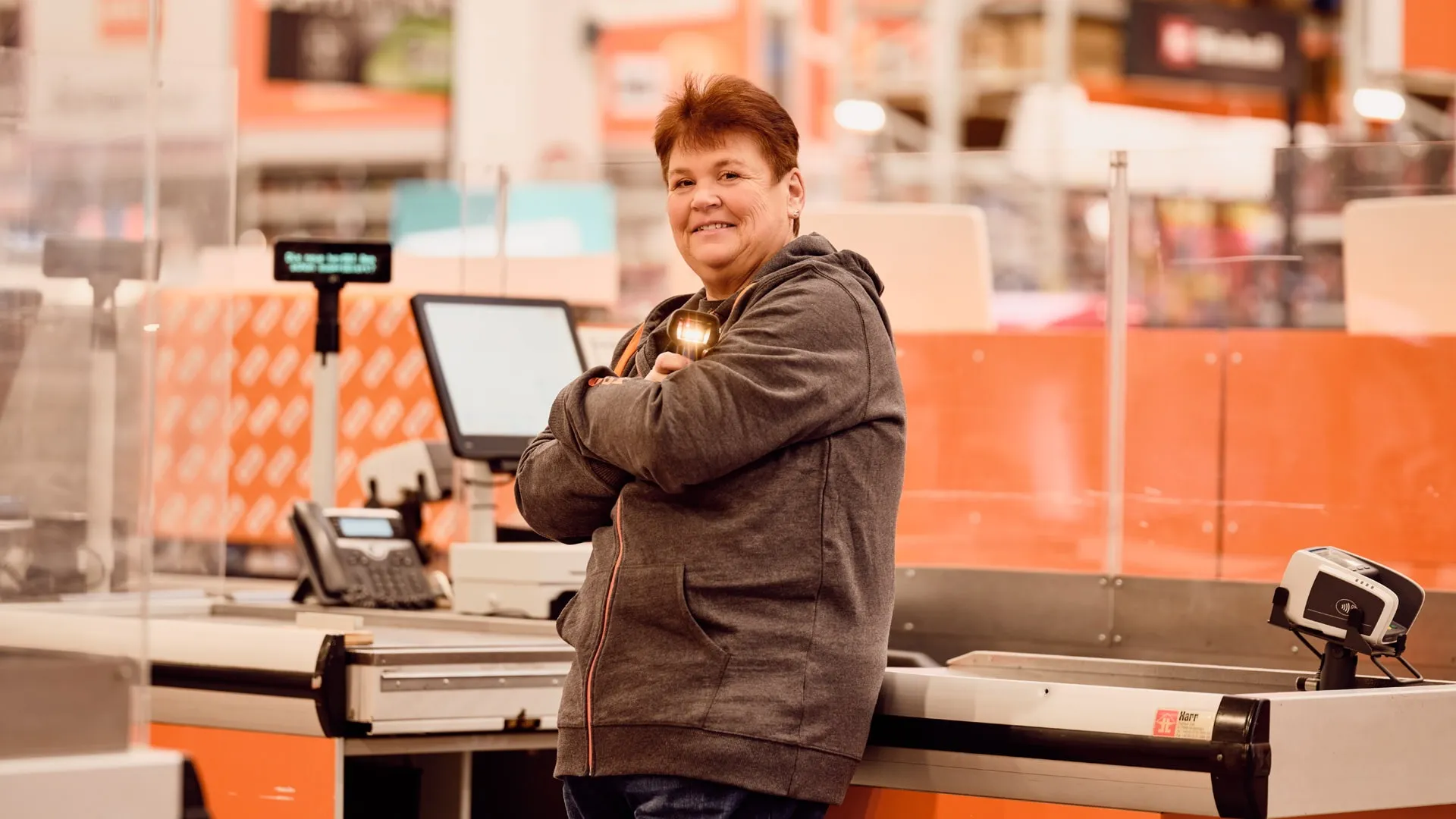 Ein Mitarbeiter von OBI AT GmbH steht lächelnd an der Kasse im Baumarkt.