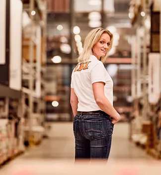 Eine OBI-Mitarbeiterin in einem Lagergang, lächelnd in die Kamera.