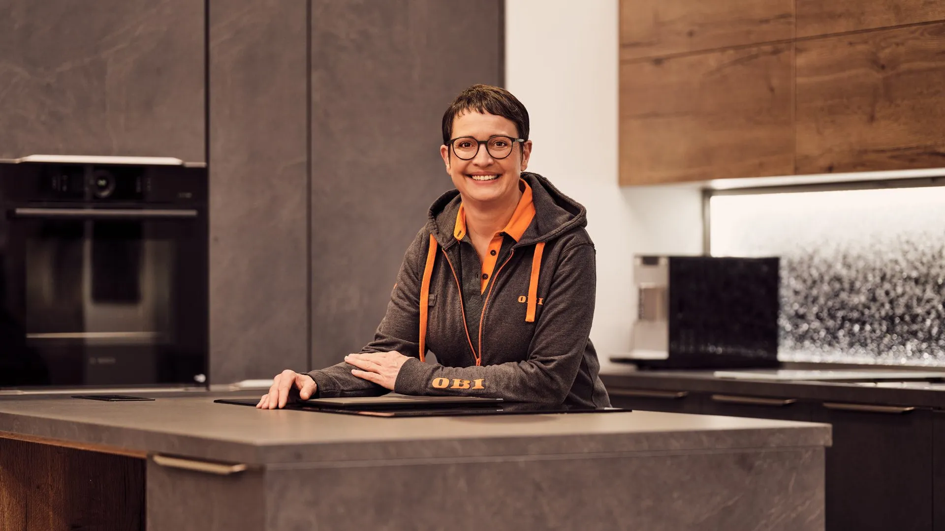 Mitarbeiterin von OBI AT GmbH lächelt freundlich in moderner Küchenumgebung und lädt Dich zum Team ein.