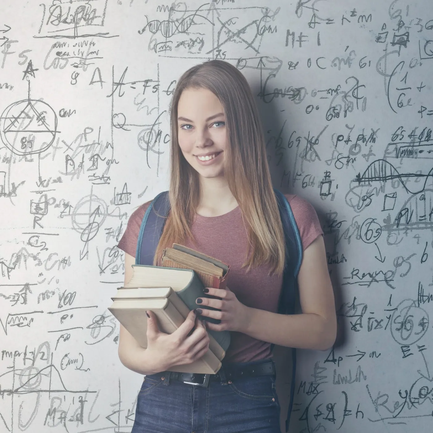 Eine junge Frau mit langen Haaren hält Bücher und lächelt vor einer Tafel mit mathematischen Formeln.