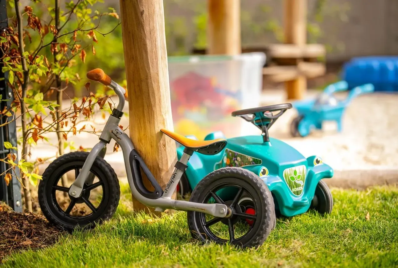 Ein Laufrad und ein Spielauto stehen auf einer Wiese in einem sonnigen Garten.