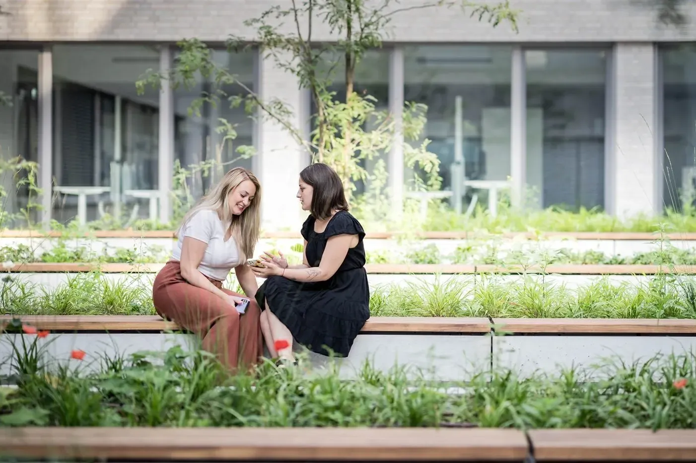 Zwei Frauen sitzen in einem grünen Innenhof und unterhalten sich fröhlich, ideal für entspannte Pausen bei opta data.