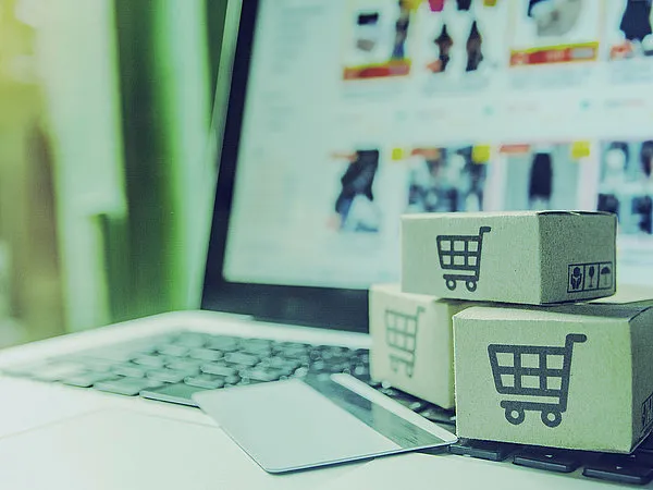 Ein Laptop mit geöffneter Einkaufsseite, Kartons mit Einkaufswagen-Symbolen und eine Kreditkarte im Vordergrund.