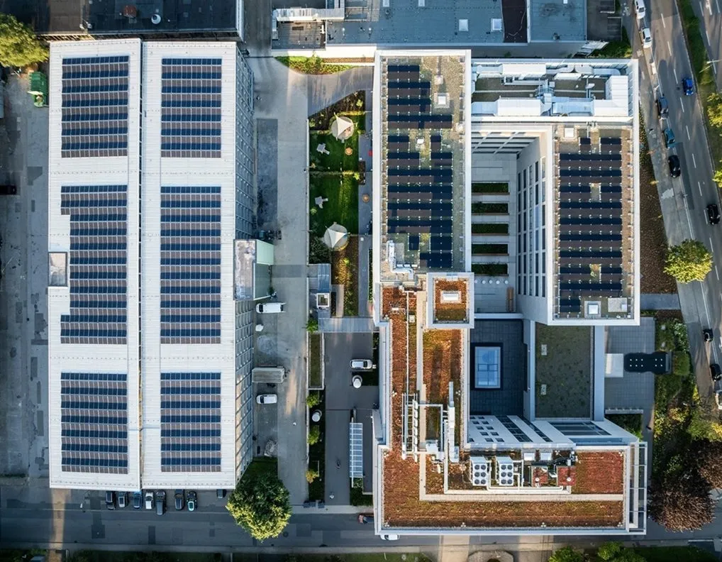 Luftaufnahme von Gebäuden mit Solarpaneelen auf den Dächern der opta data Gruppe, umgeben von Grünflächen und Straßen.