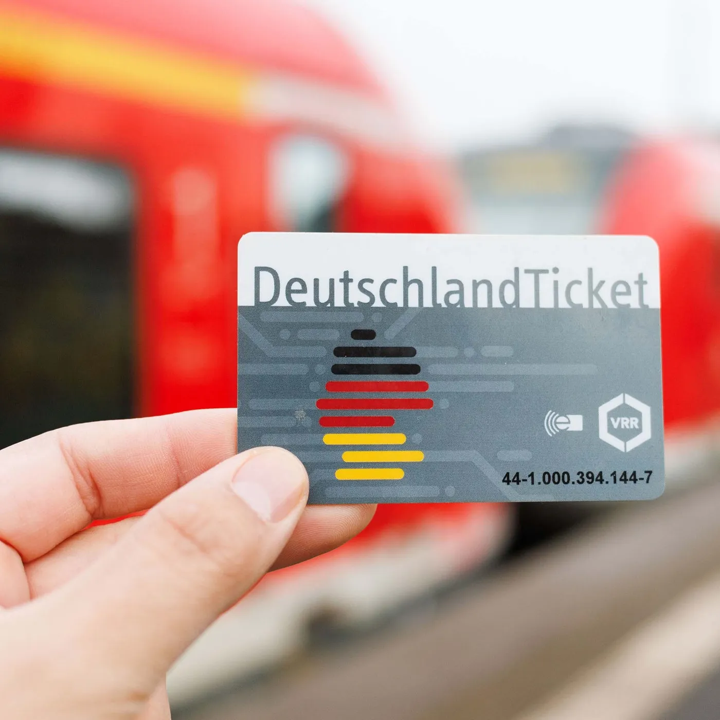 Hand hält ein DeutschlandTicket vor einem roten Zug im Hintergrund, symbolisch für Mobilität im Gesundheitssektor.