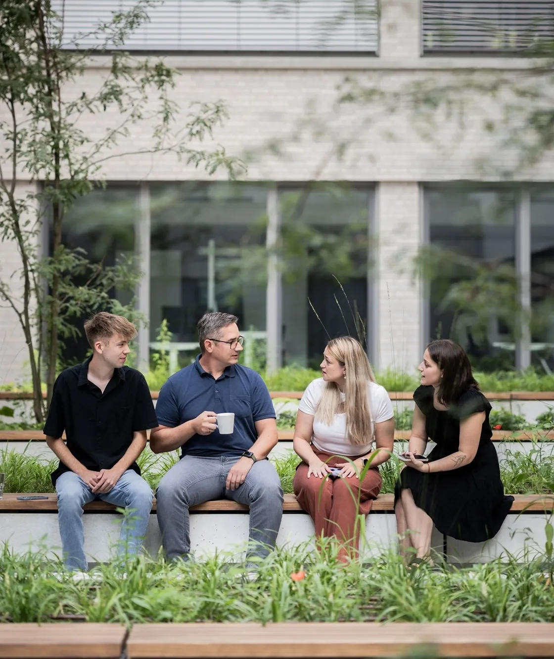 Vier Kollegen unterhalten sich entspannt in einem grünen Innenhof auf dem Campus von opta data.