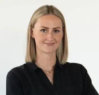 Junge Frau mit blonder Bob-Frisur und schwarzem Hemd lächelt selbstbewusst mit verschränkten Armen in die Kamera.