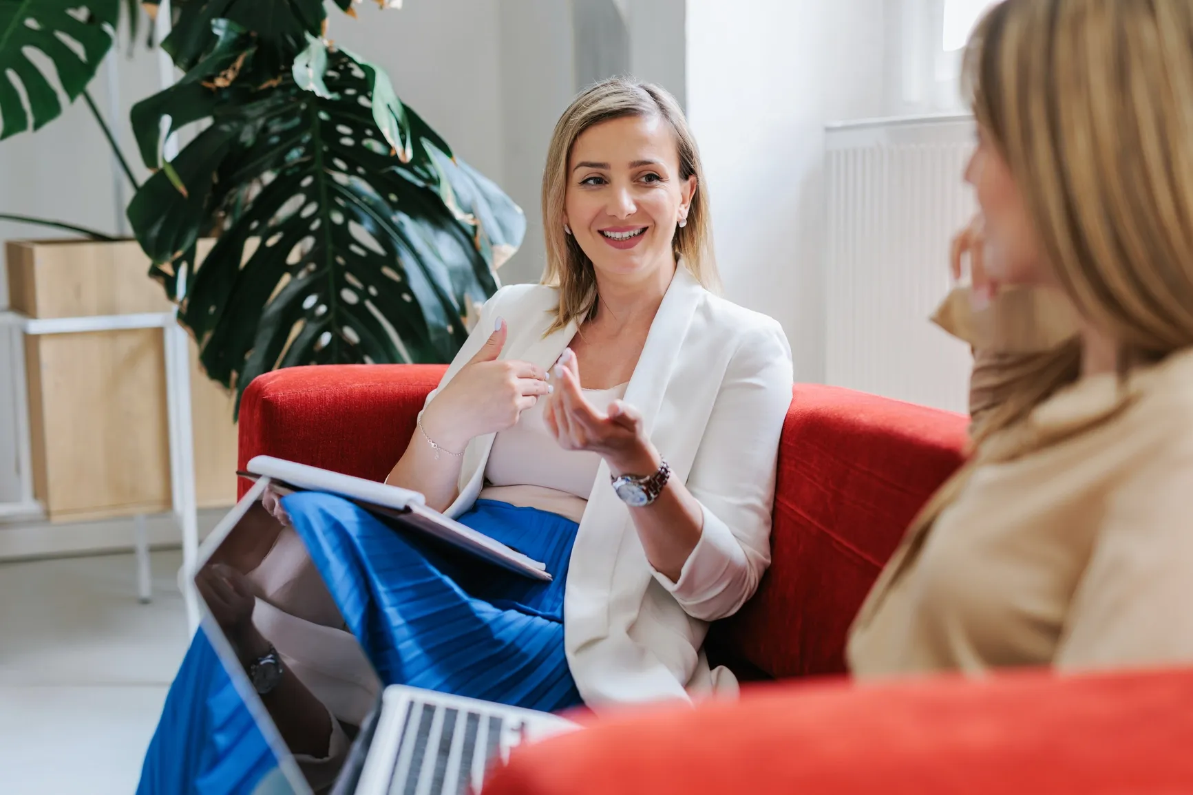 Two colleagues chatting and smiling on a red couch, laptops open, in a relaxed Ratepay office setting.