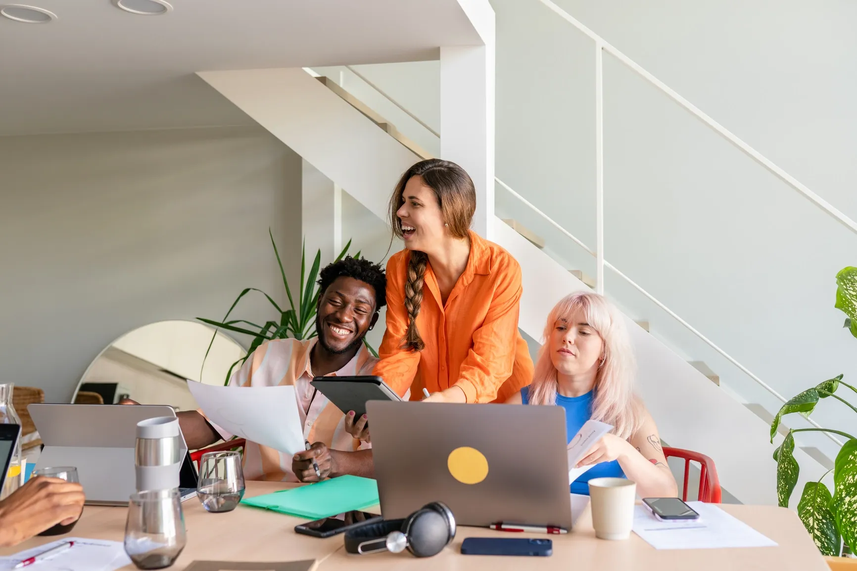 Three young colleagues laughing and working together at a bright office table, showing Ratepay’s friendly team vibe.