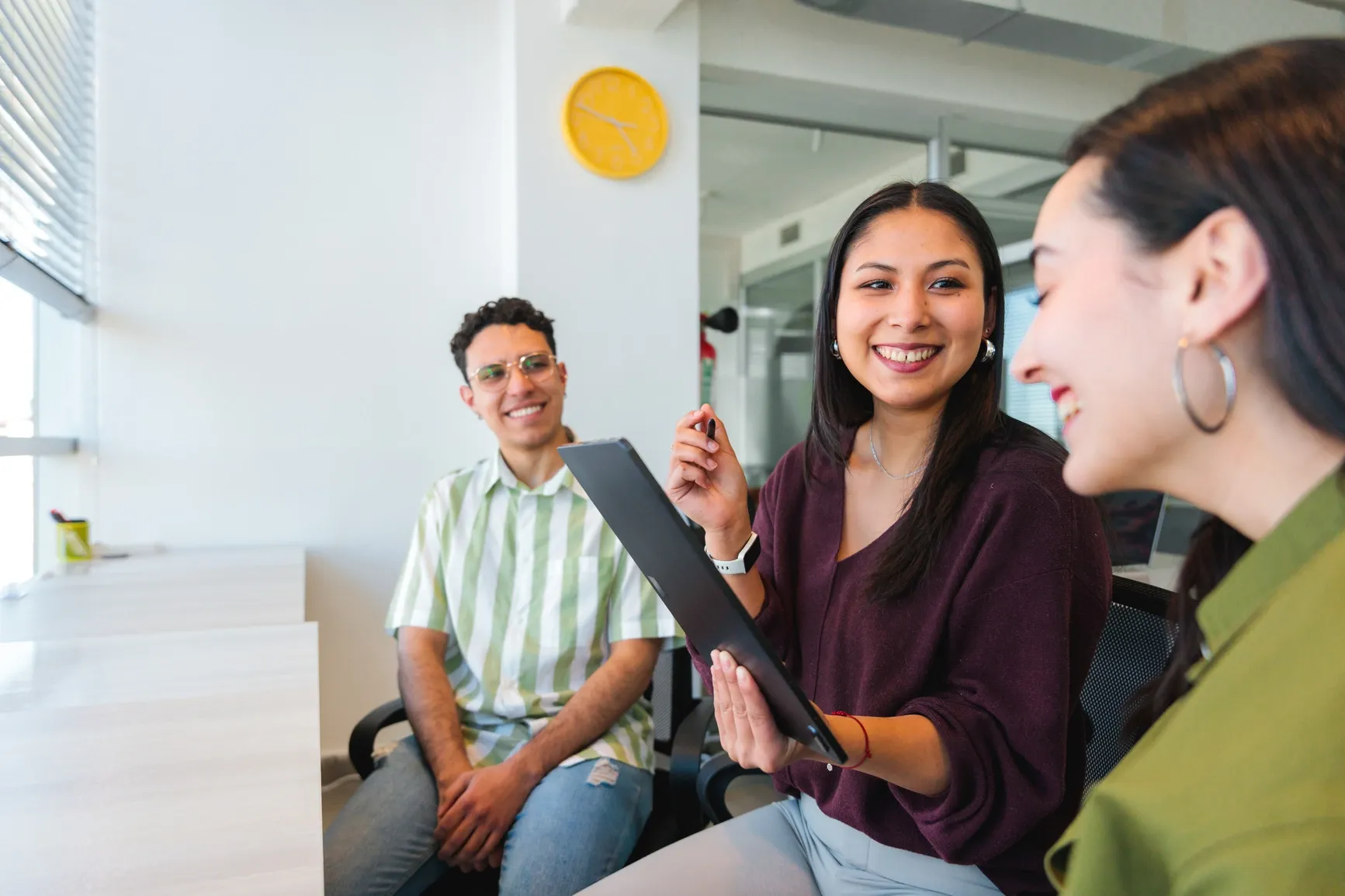 Three young colleagues chatting and smiling together in a bright, modern Ratepay office, holding a tablet.