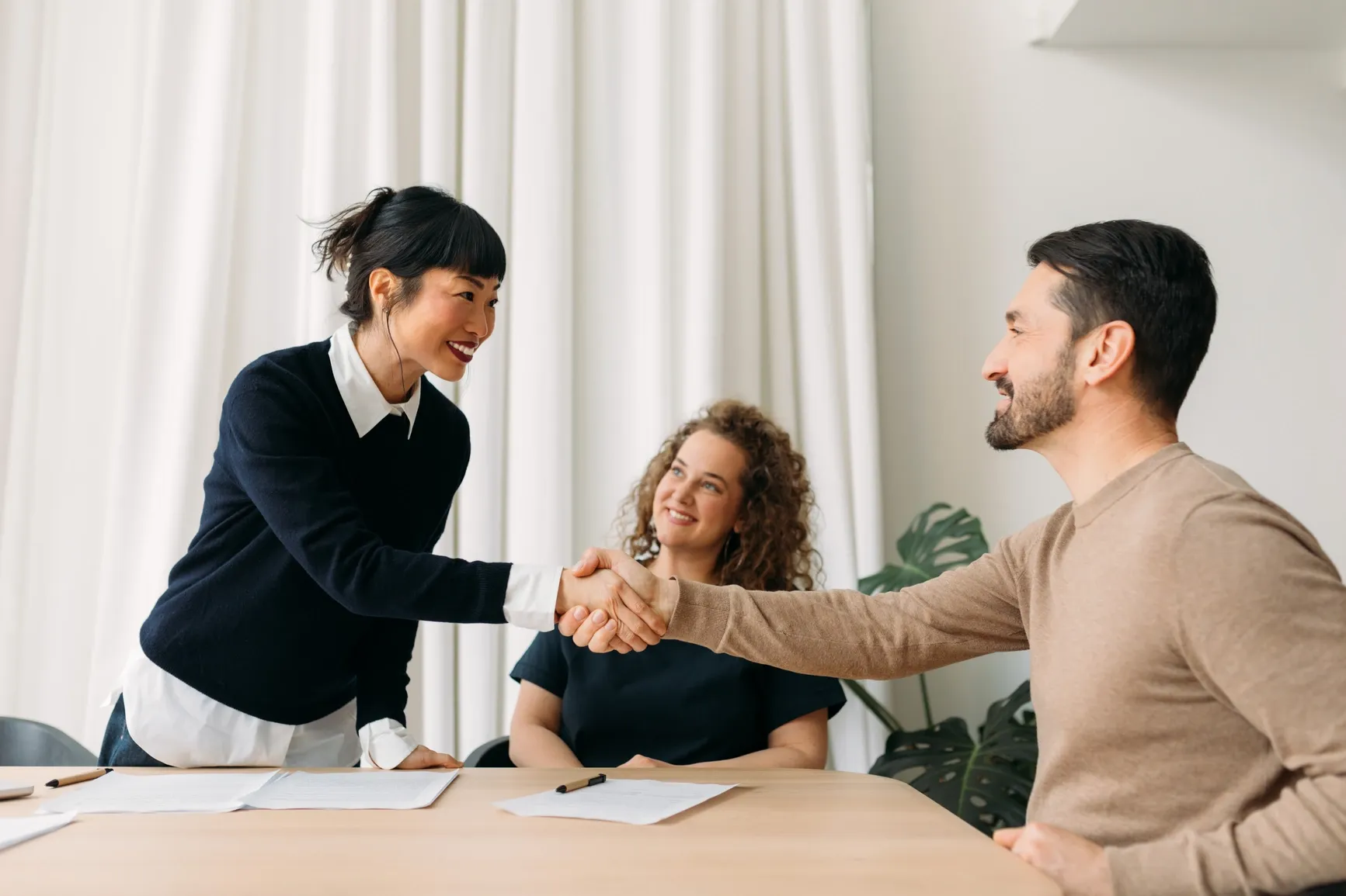 Two people smiling and shaking hands in a friendly job interview at ratepay GmbH, with a relaxed team vibe.