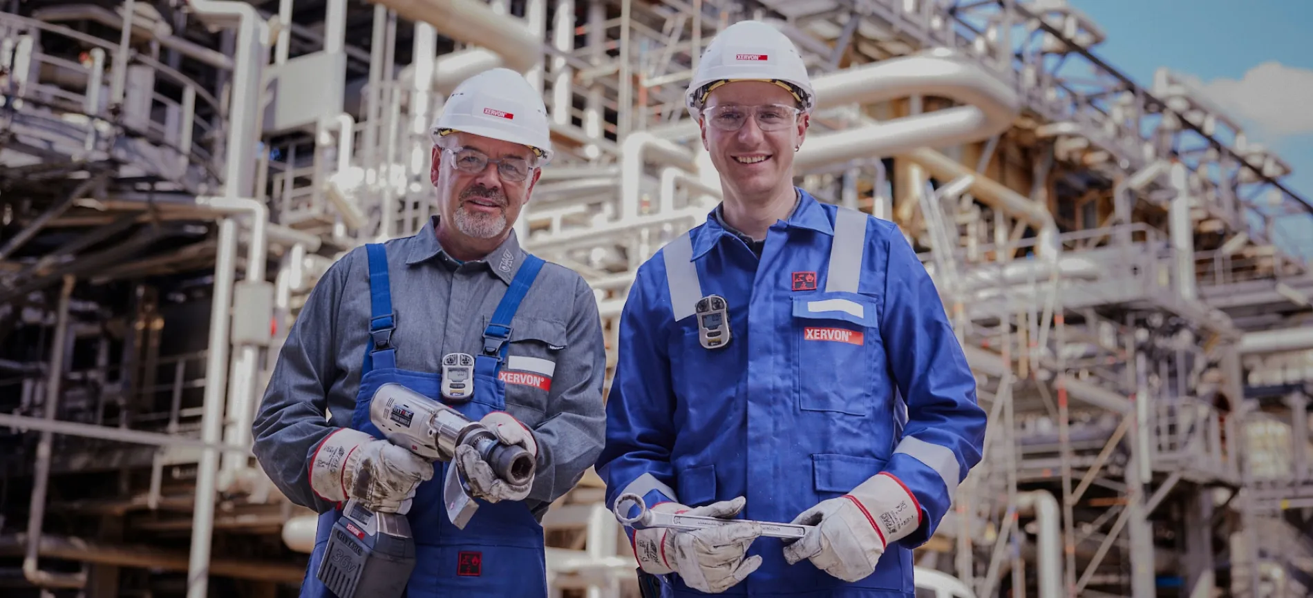 Zwei REMONDIS-Mitarbeiter in Schutzkleidung arbeiten lächelnd mit Werkzeug an einer Industrieanlage.