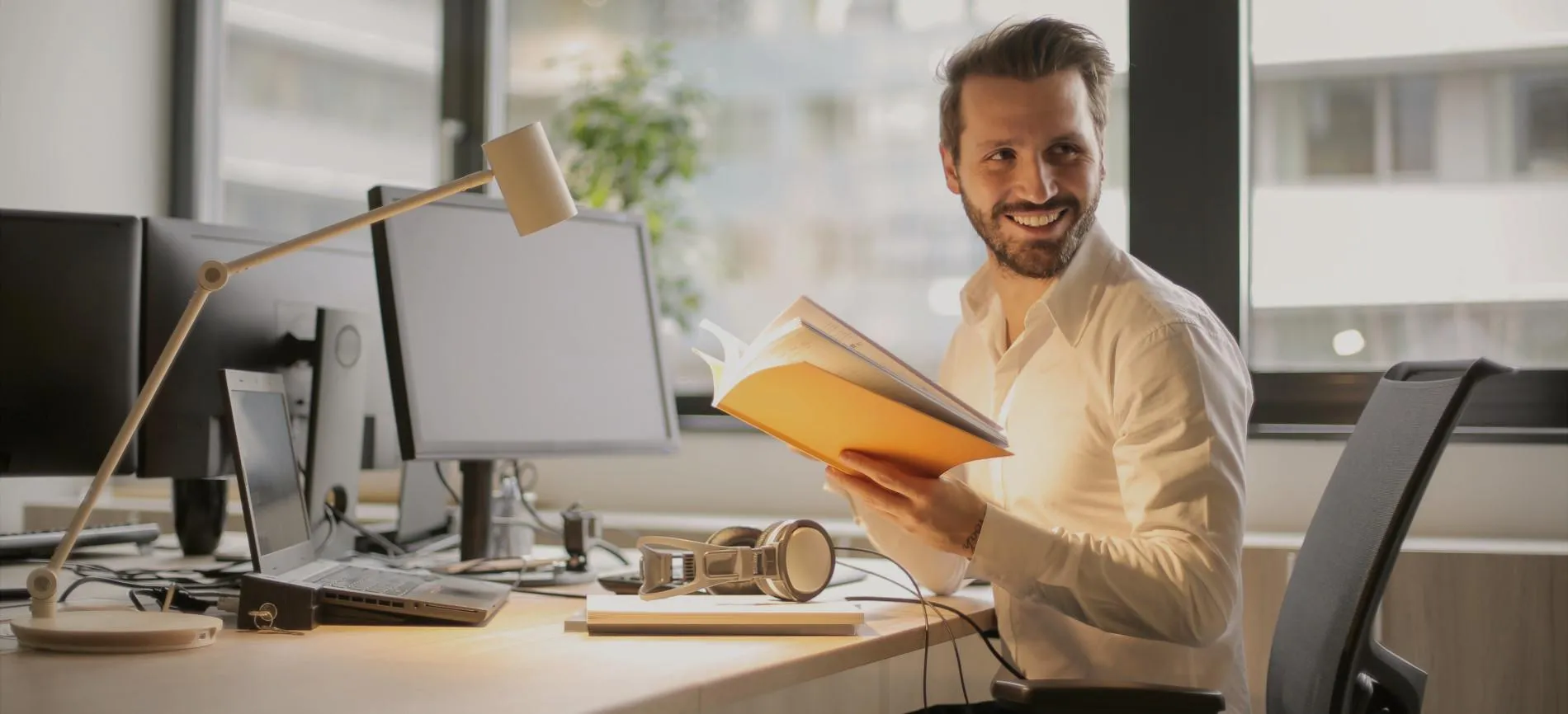Lächelnder Mitarbeiter am Schreibtisch liest Unterlagen im modernen Büro bei REMONDIS im Bereich Energie und Versorgung.