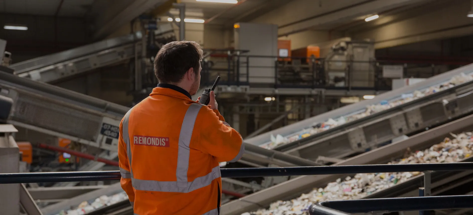 Mitarbeiter in REMONDIS-Arbeitskleidung überwacht mit Funkgerät die Sortieranlage für Recyclingmaterialien.