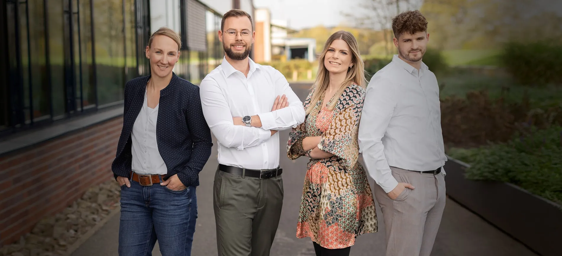Vier junge Kolleg:innen stehen lächelnd und selbstbewusst vor dem Firmengebäude von REMONDIS Industrie Service.
