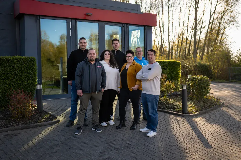 Eine Gruppe von sieben lächelnden Menschen steht vor einem Gebäude von REMONDIS Maintenance & Services GmbH & Co. KG.