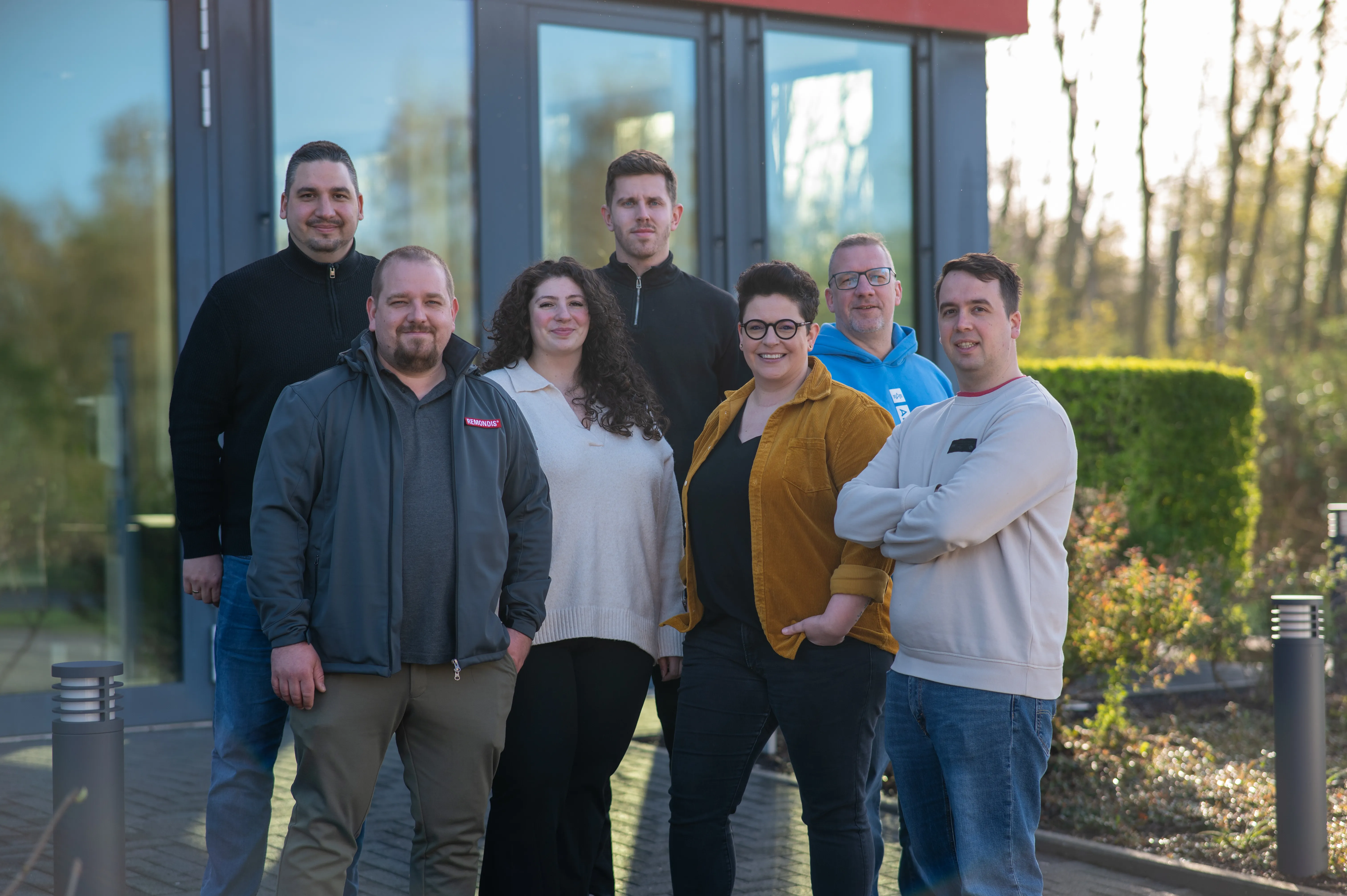 Eine Gruppe von sieben lächelnden Menschen steht vor einem Gebäude von REMONDIS Maintenance & Services GmbH & Co. KG.