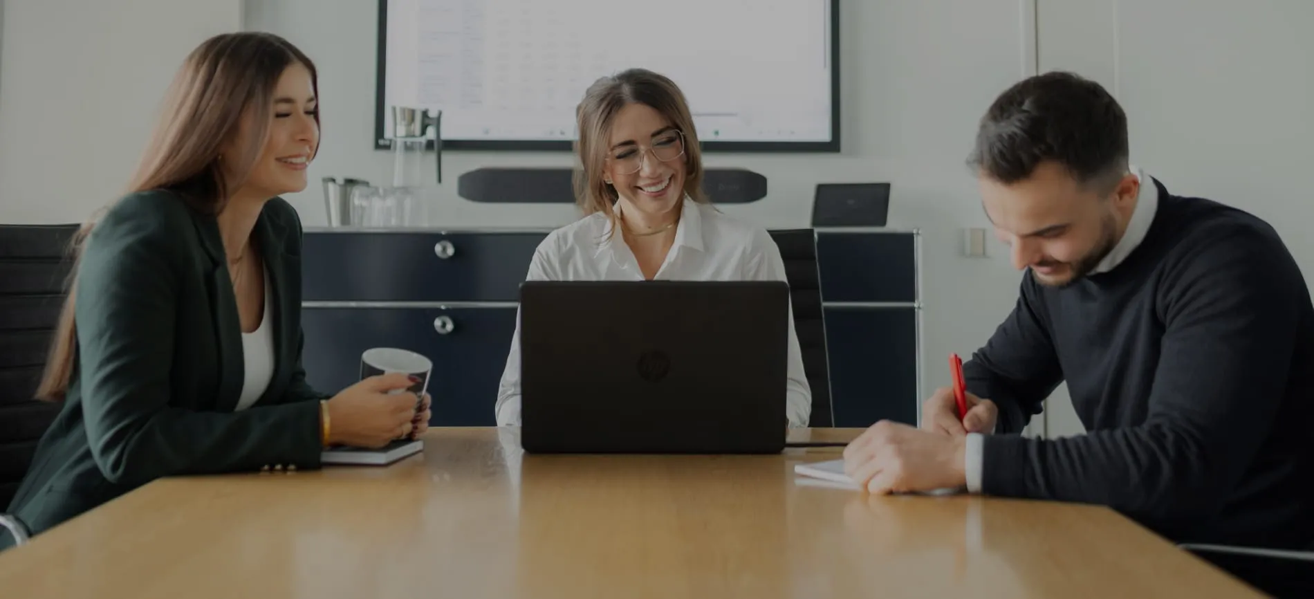 Drei junge Kollegen lachen gemeinsam bei einem Meeting im Büro – Du kannst Teil dieses Teams werden.