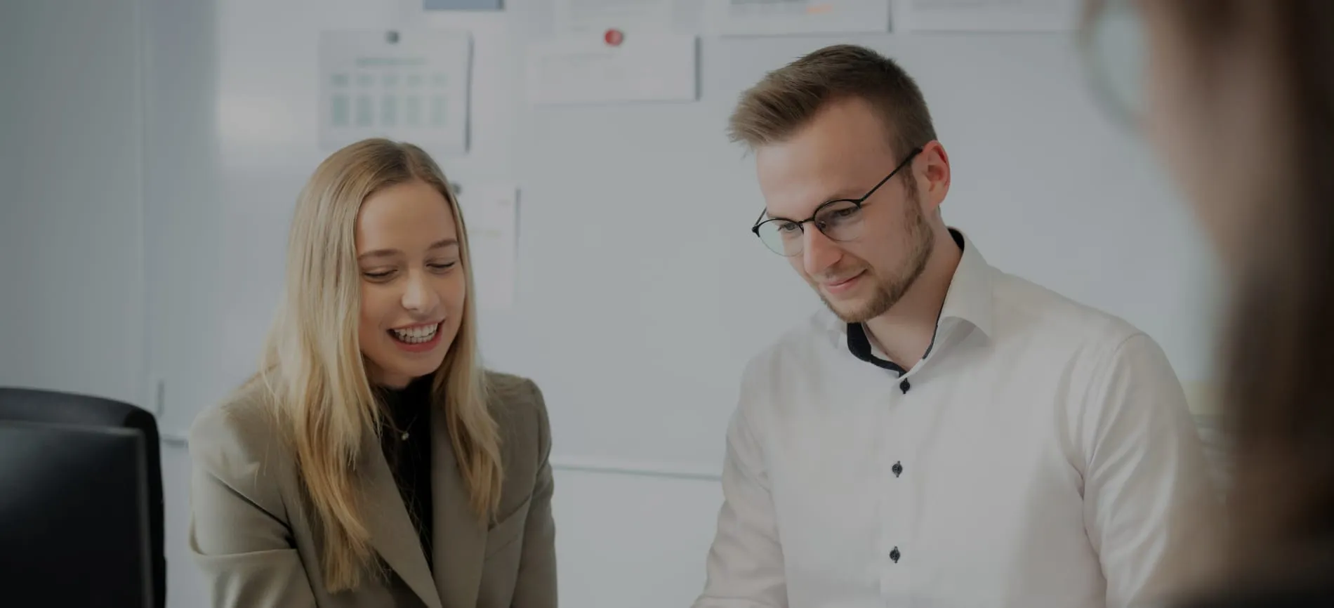 Zwei junge Kollegen lächeln und arbeiten gemeinsam an einem Projekt im modernen Büro bei REMONDIS Production GmbH.
