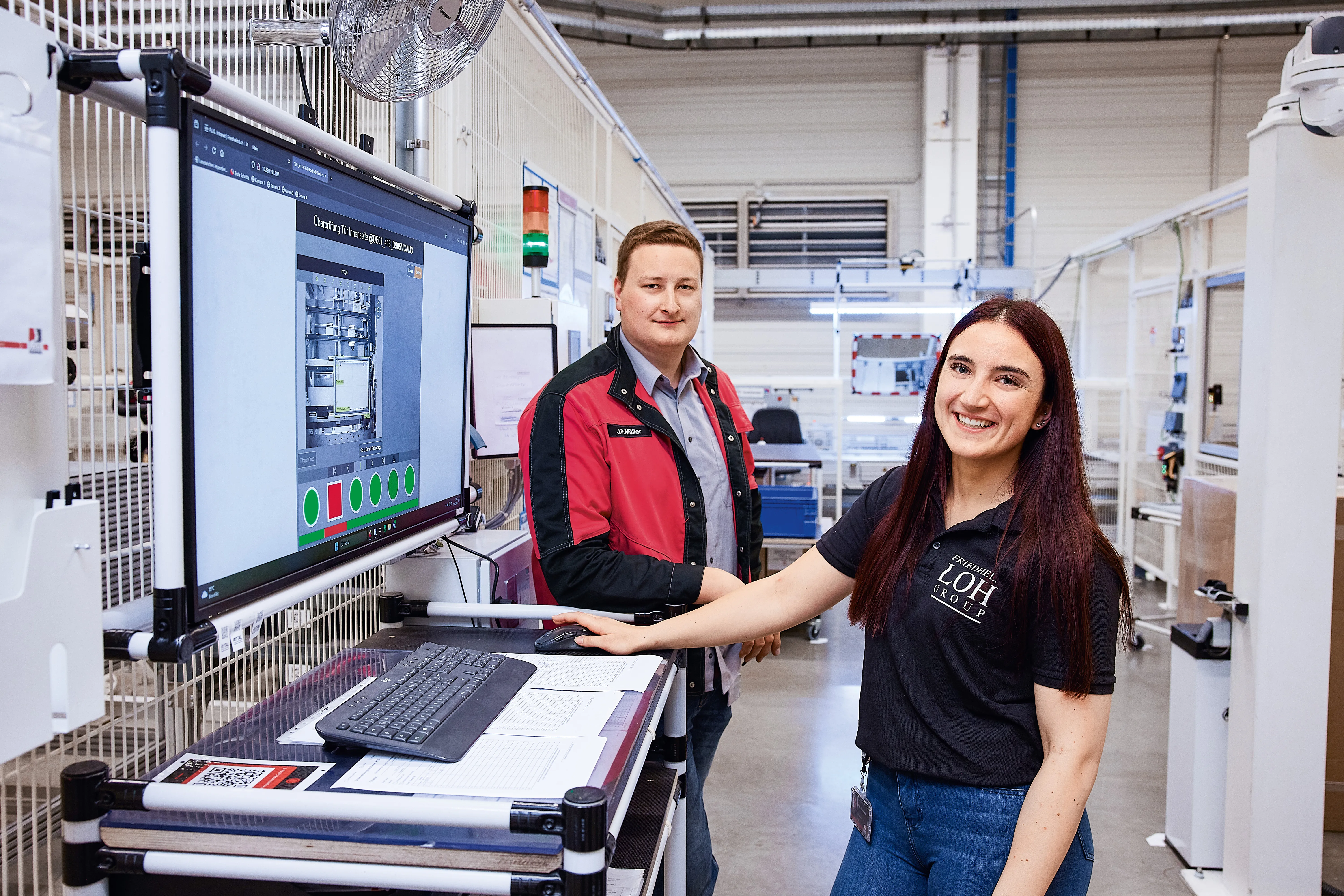 Two Rittal employees happily collaborating in a tech workspace, checking data on a large screen.