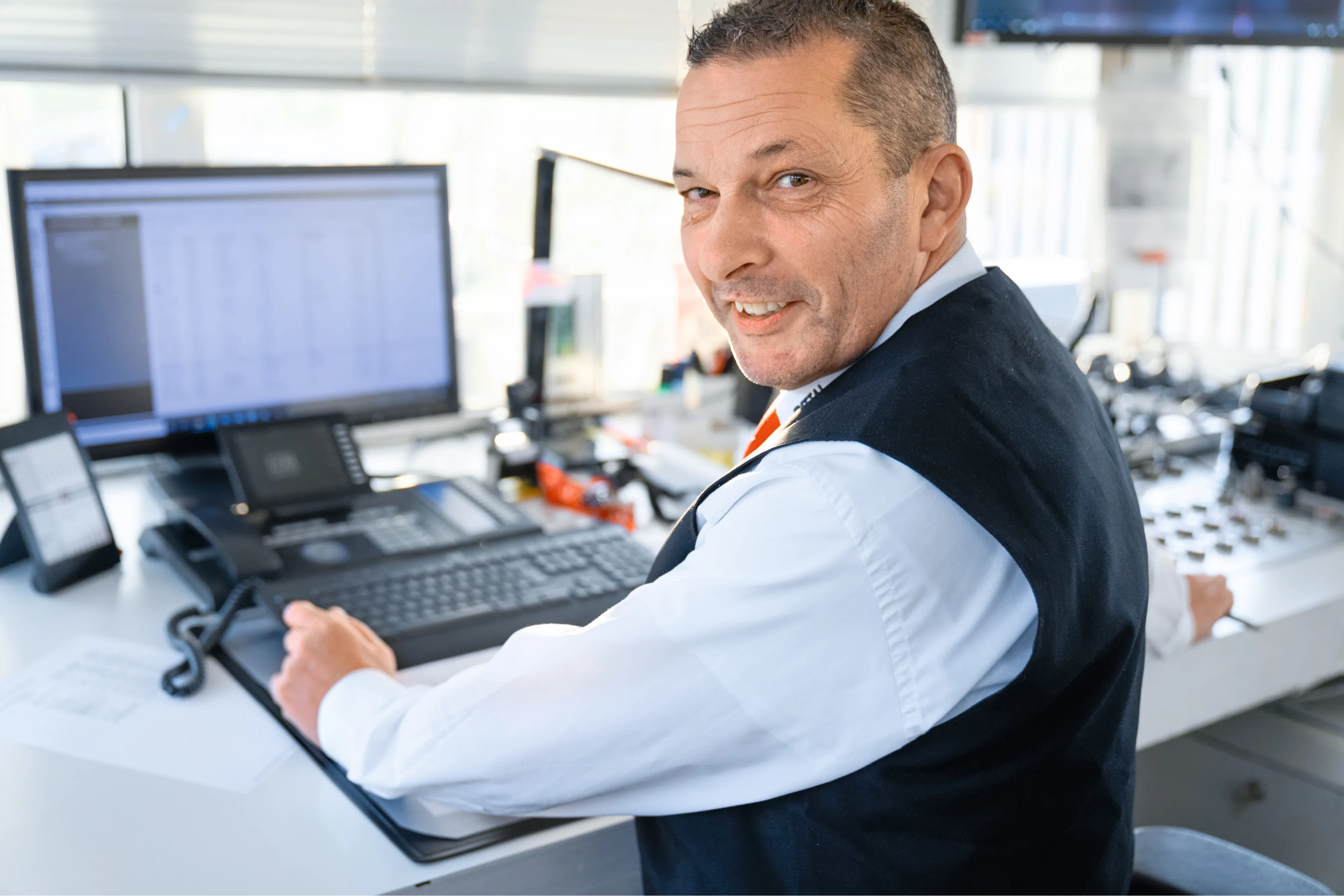 Ein lächelnder Mann arbeitet am Computer in einem modernen Büro bei Rittal GmbH & Co. KG im IT-Bereich.