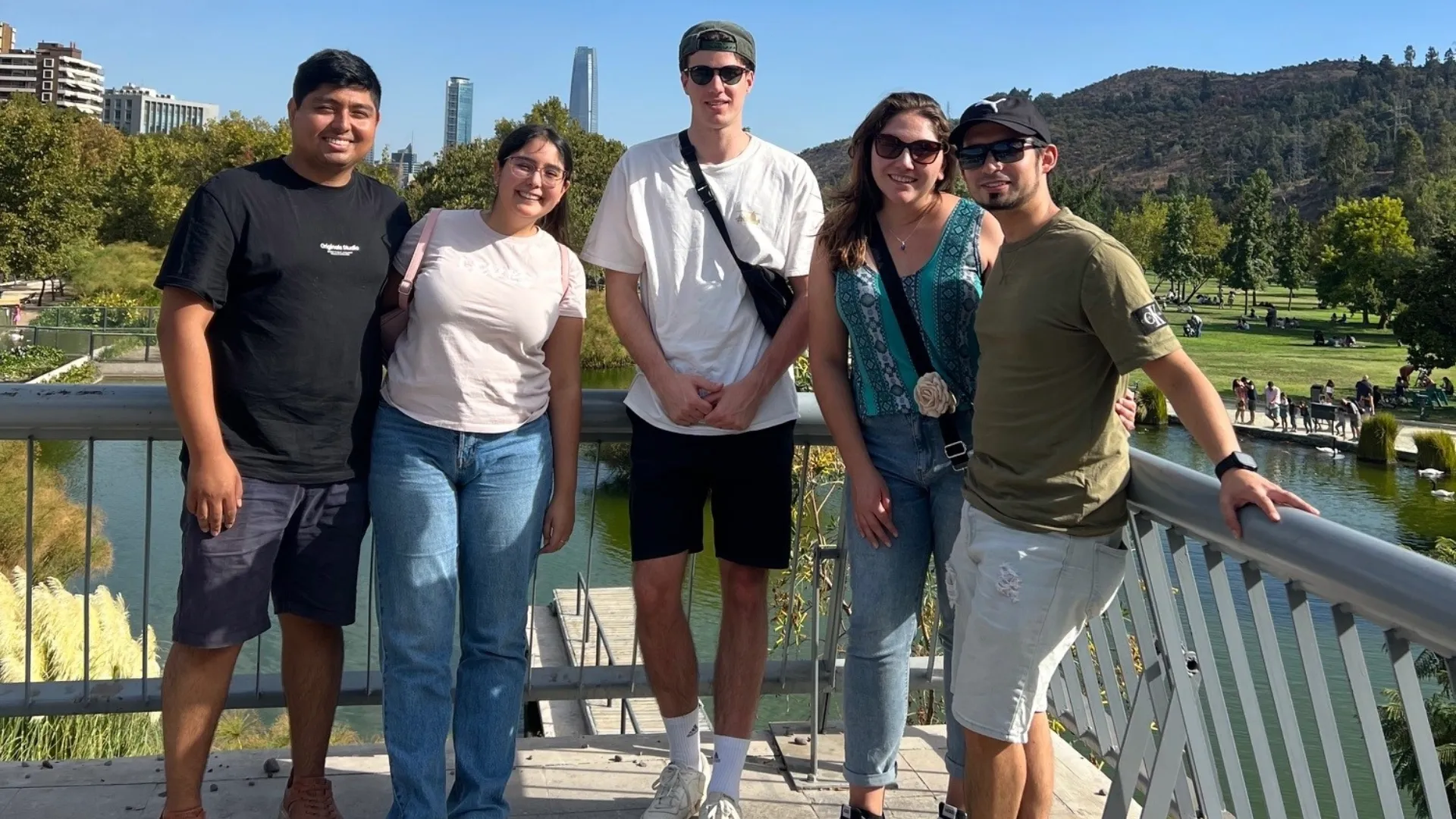 A group of five young adults enjoying a sunny day in the park, with a city skyline and lush greenery in the background.