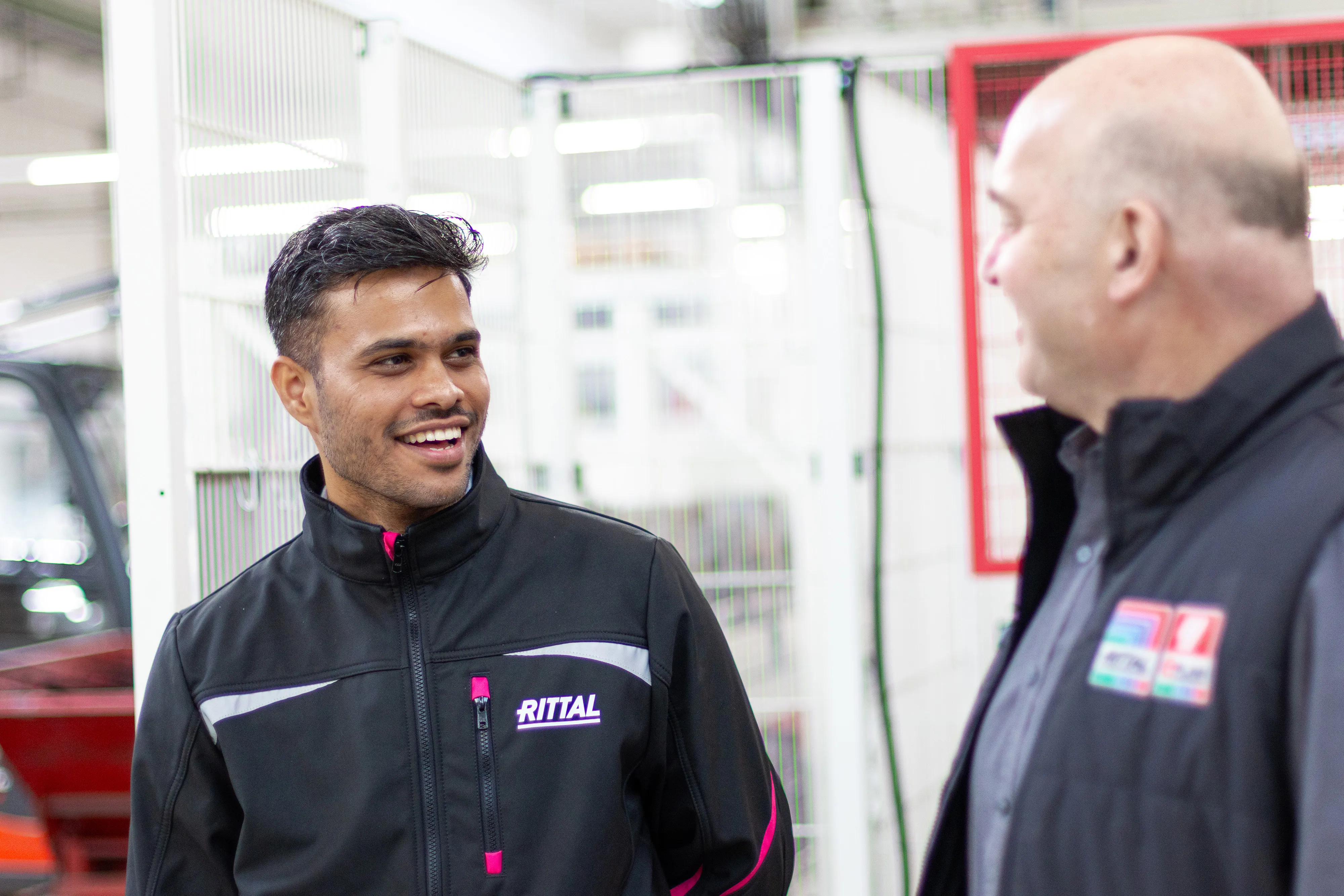 A cheerful employee in a Rittal jacket welcomes you to the high-tech production floor.