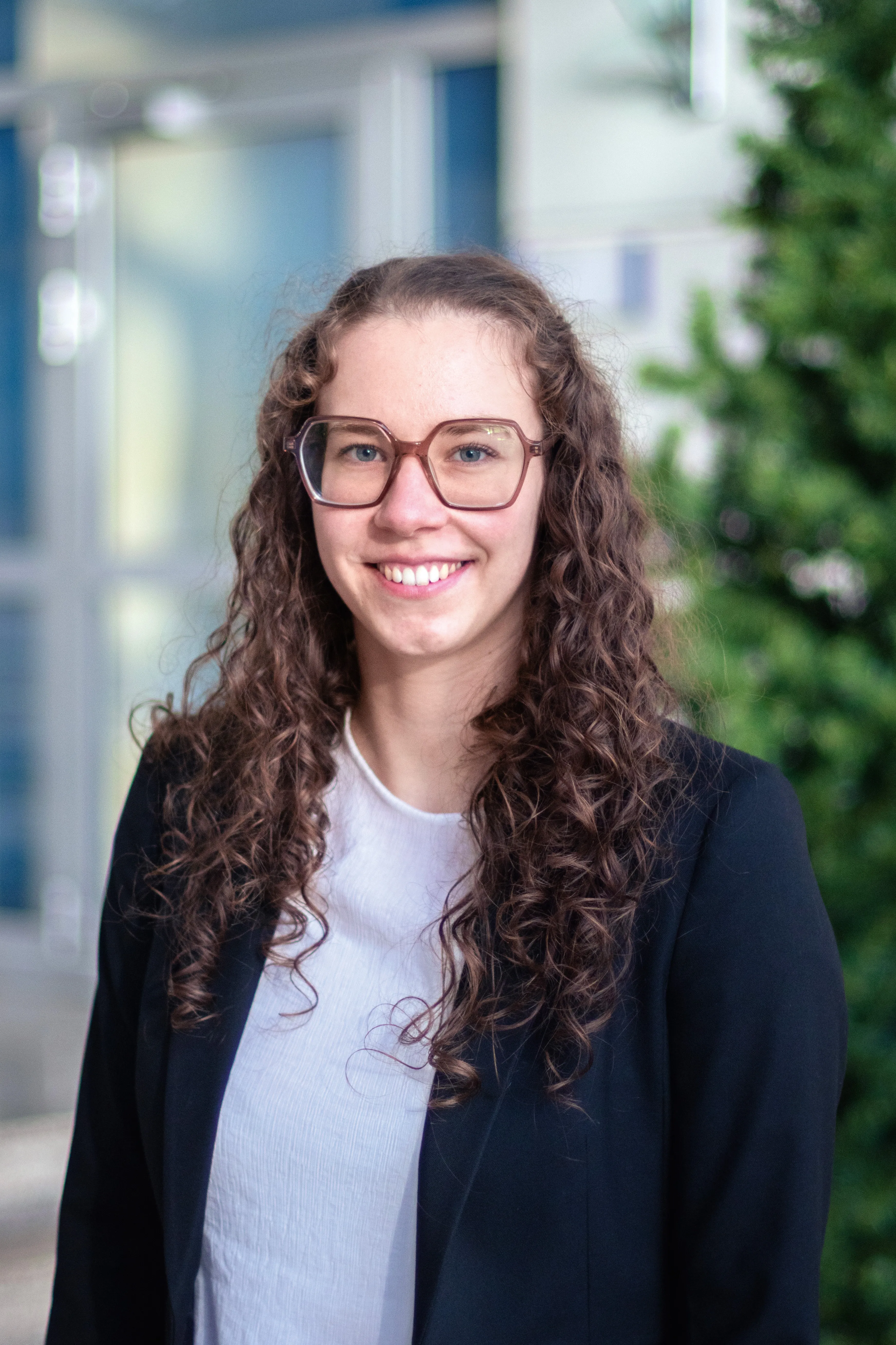 Eine lächelnde Frau mit lockigem Haar und Brille in einem Bürogebäude. Ideal für die Karrierewebsite von Rittal GmbH & Co. KG.