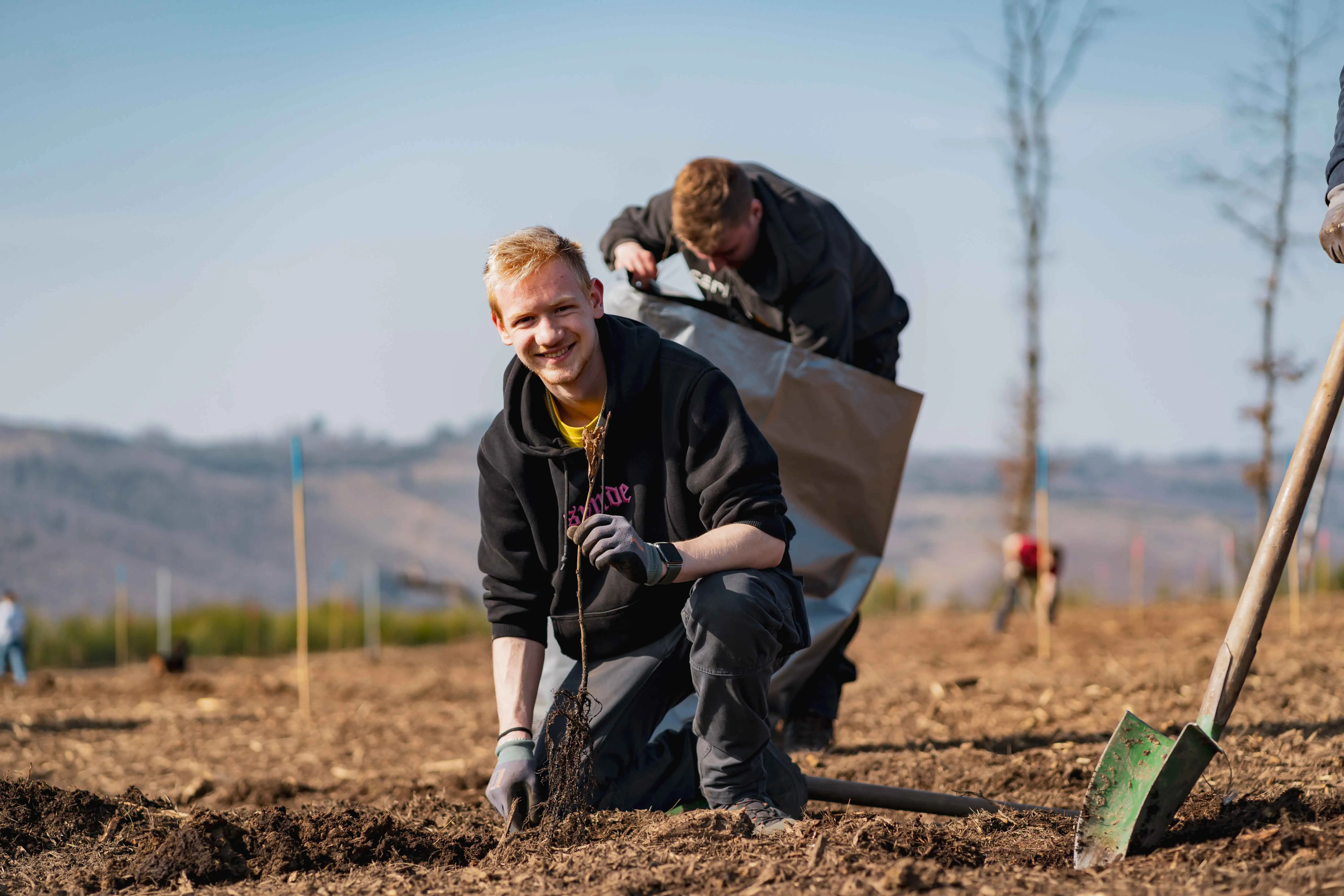 Young professionals planting trees with smiles, embracing sustainability at Rittal's environmental event.