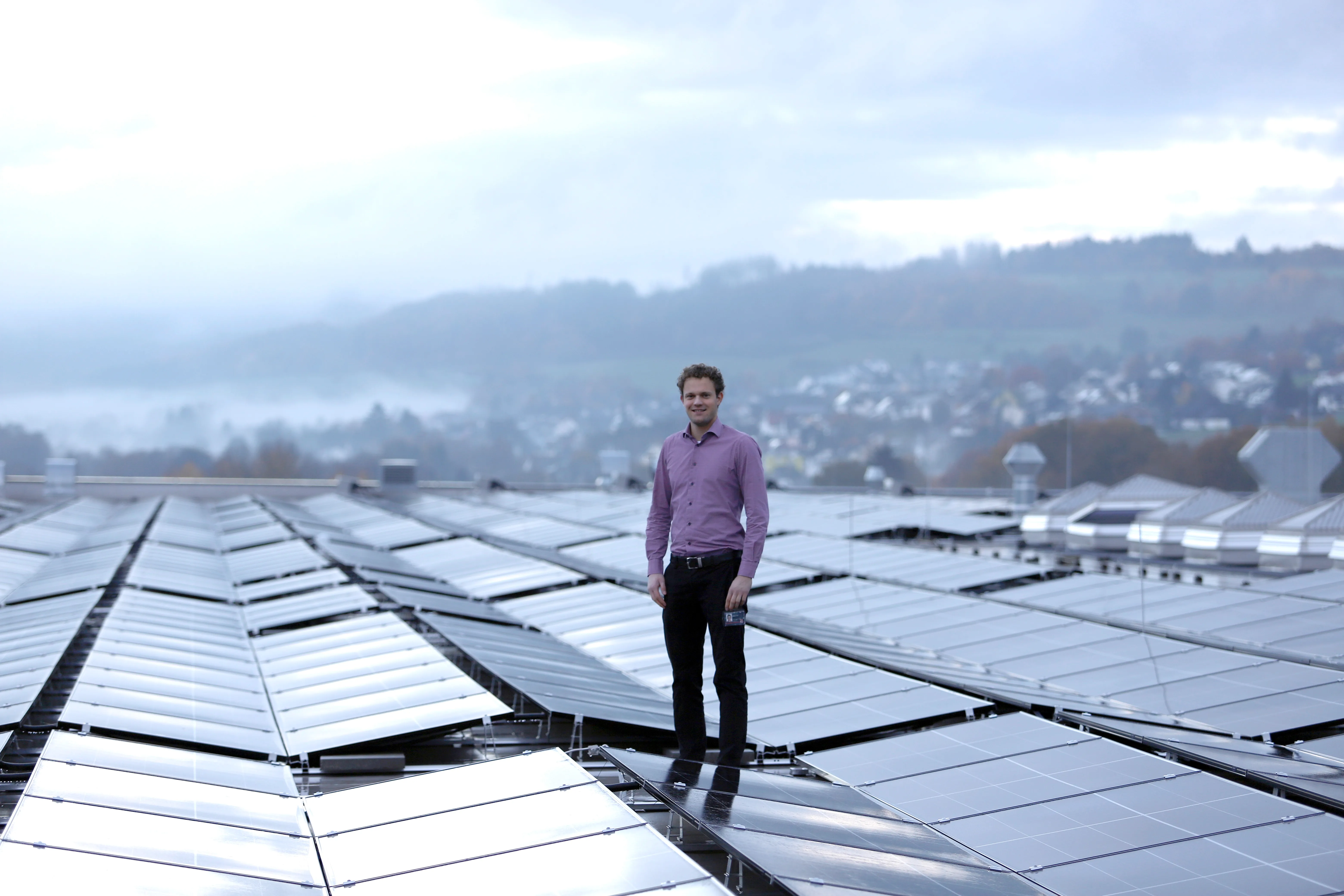 Man standing on a rooftop with solar panels, overlooking a misty landscape. Perfect for showcasing Rittal's green tech vibe!