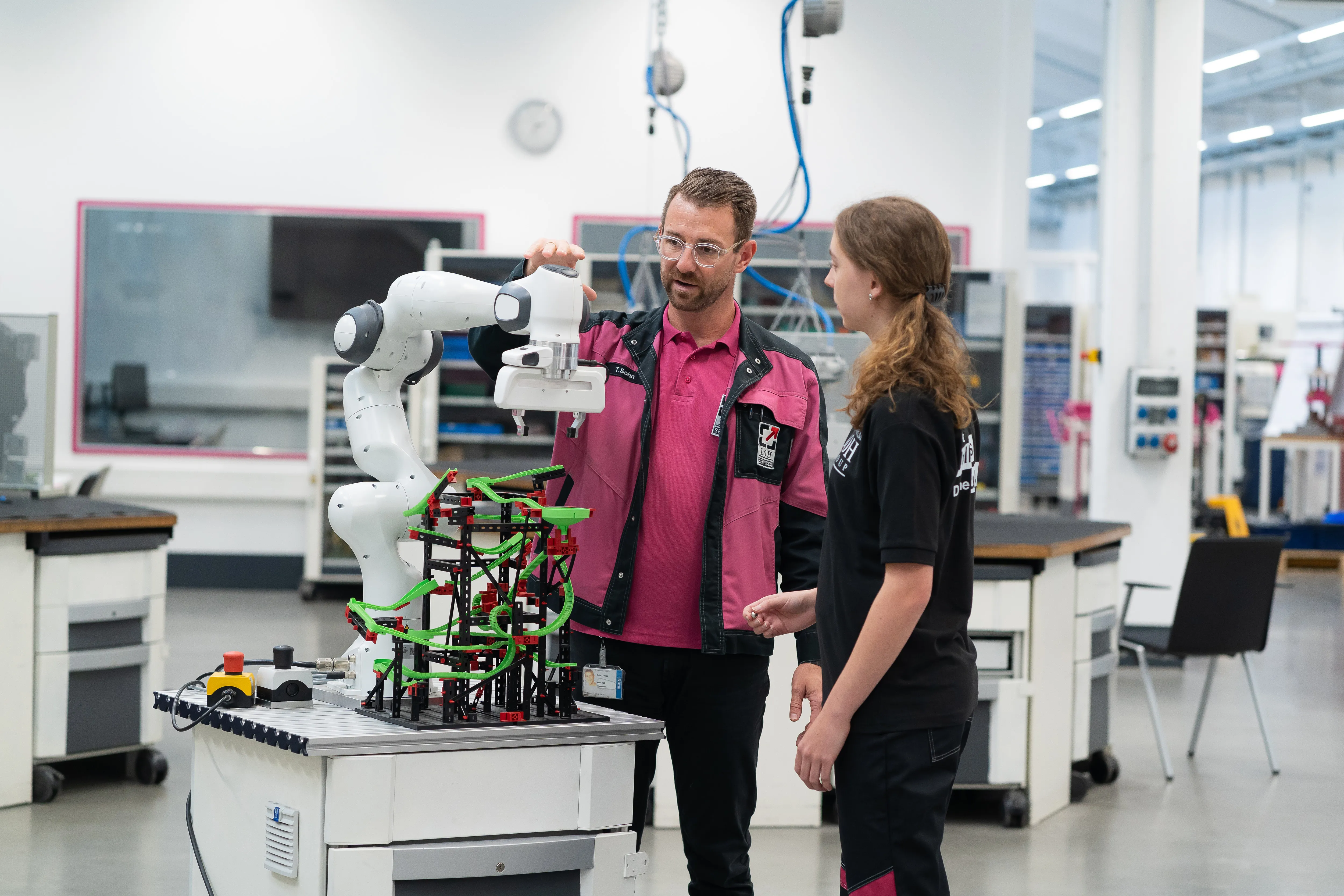 Two team members at Rittal exploring a robot's capabilities in a modern tech lab, wearing branded uniforms.