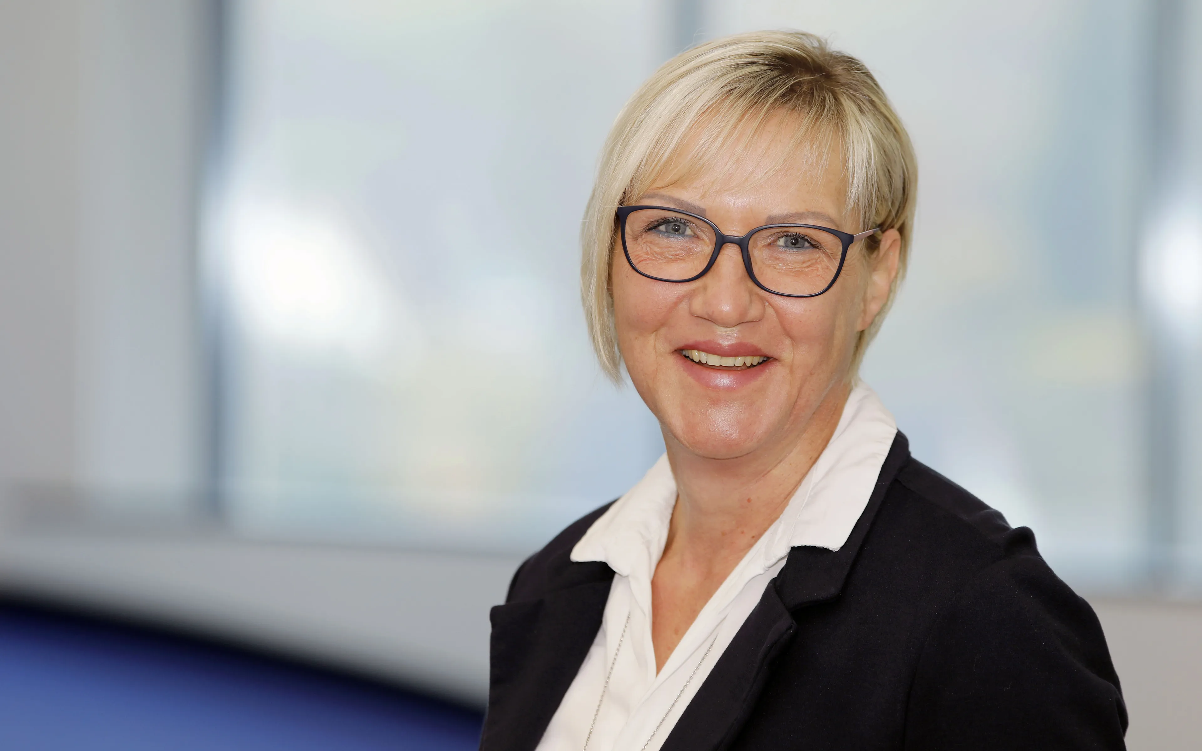 Eine lächelnde Frau mit Brille und blondem Haar in einem professionellen Umfeld. Ideal für Rittal GmbH & Co. KG.