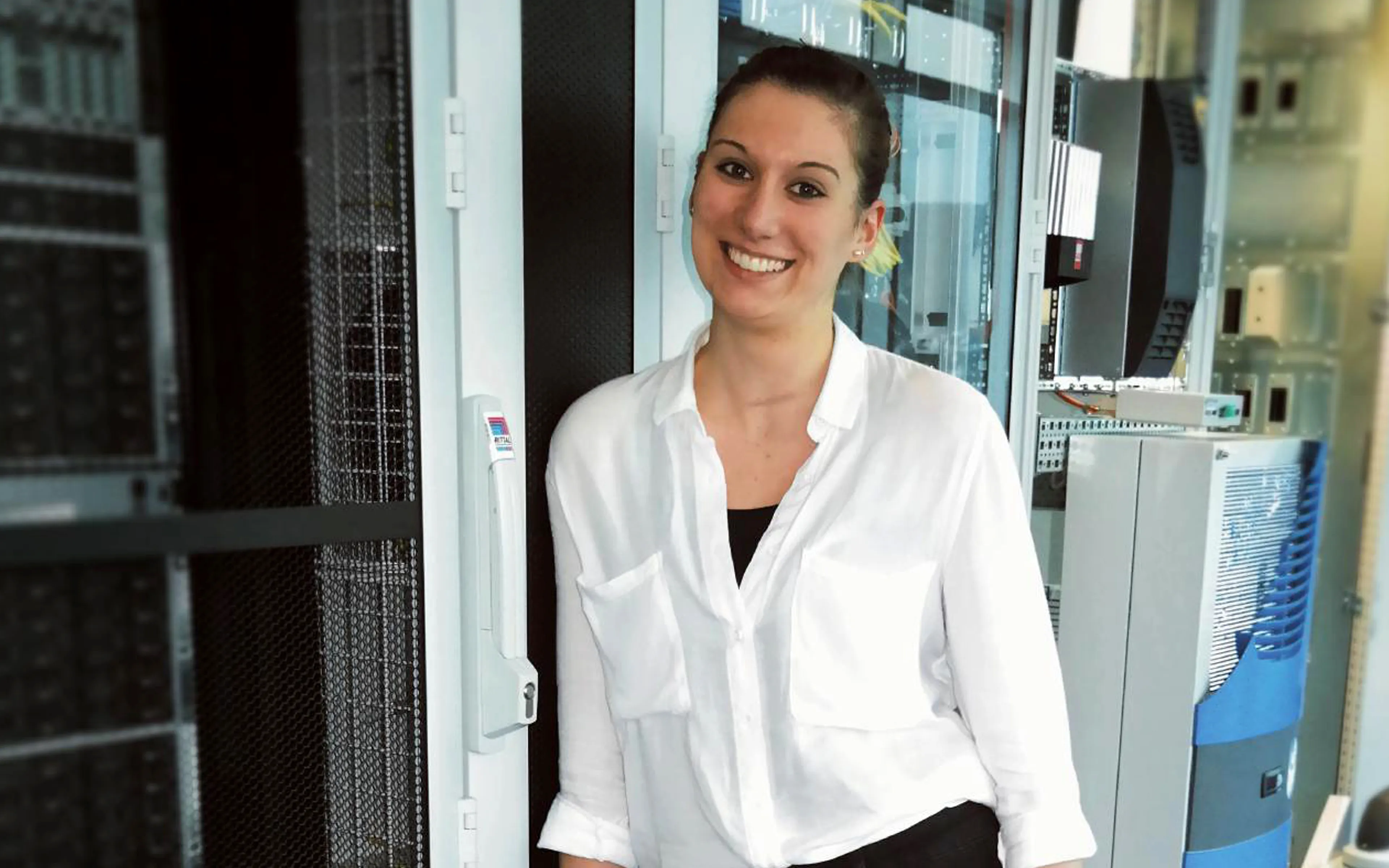 Eine Frau in weißer Bluse lächelt in einem Serverraum von Rittal GmbH & Co. KG.