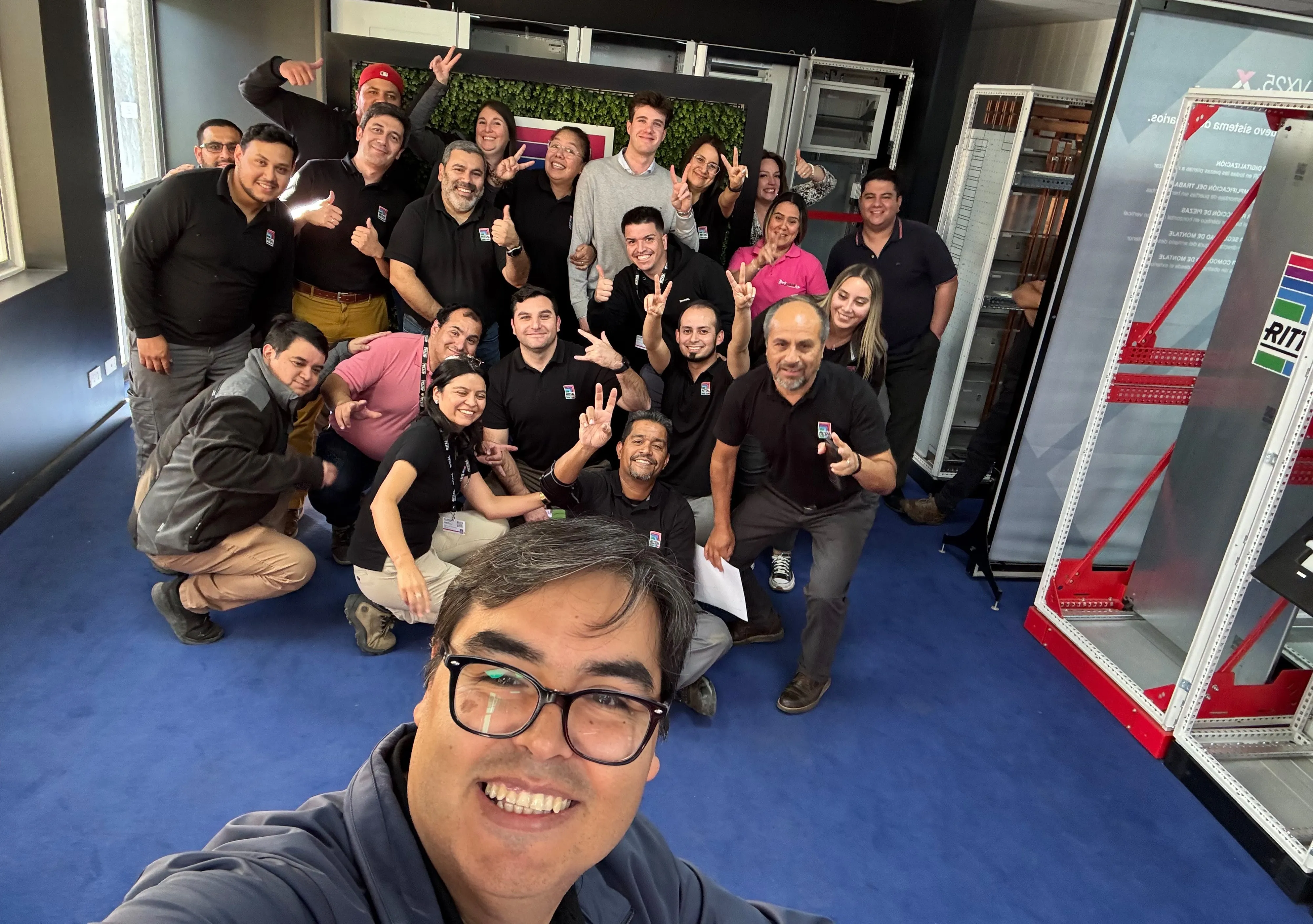 A group of cheerful Rittal team members posing together, showcasing their camaraderie in an IT workspace.