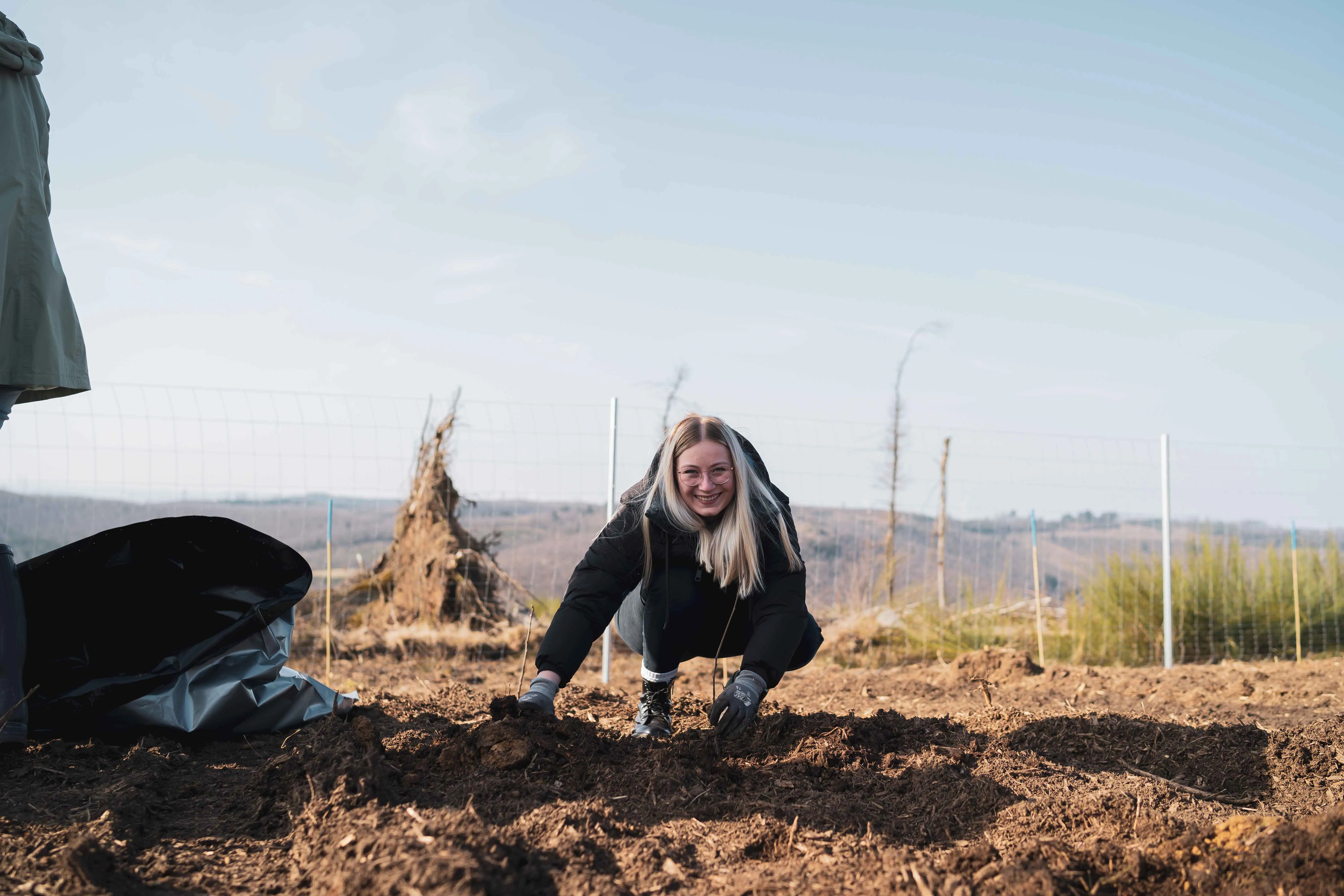 A cheerful woman planting saplings outdoors on a sunny day, showcasing Rittal’s commitment to sustainability.