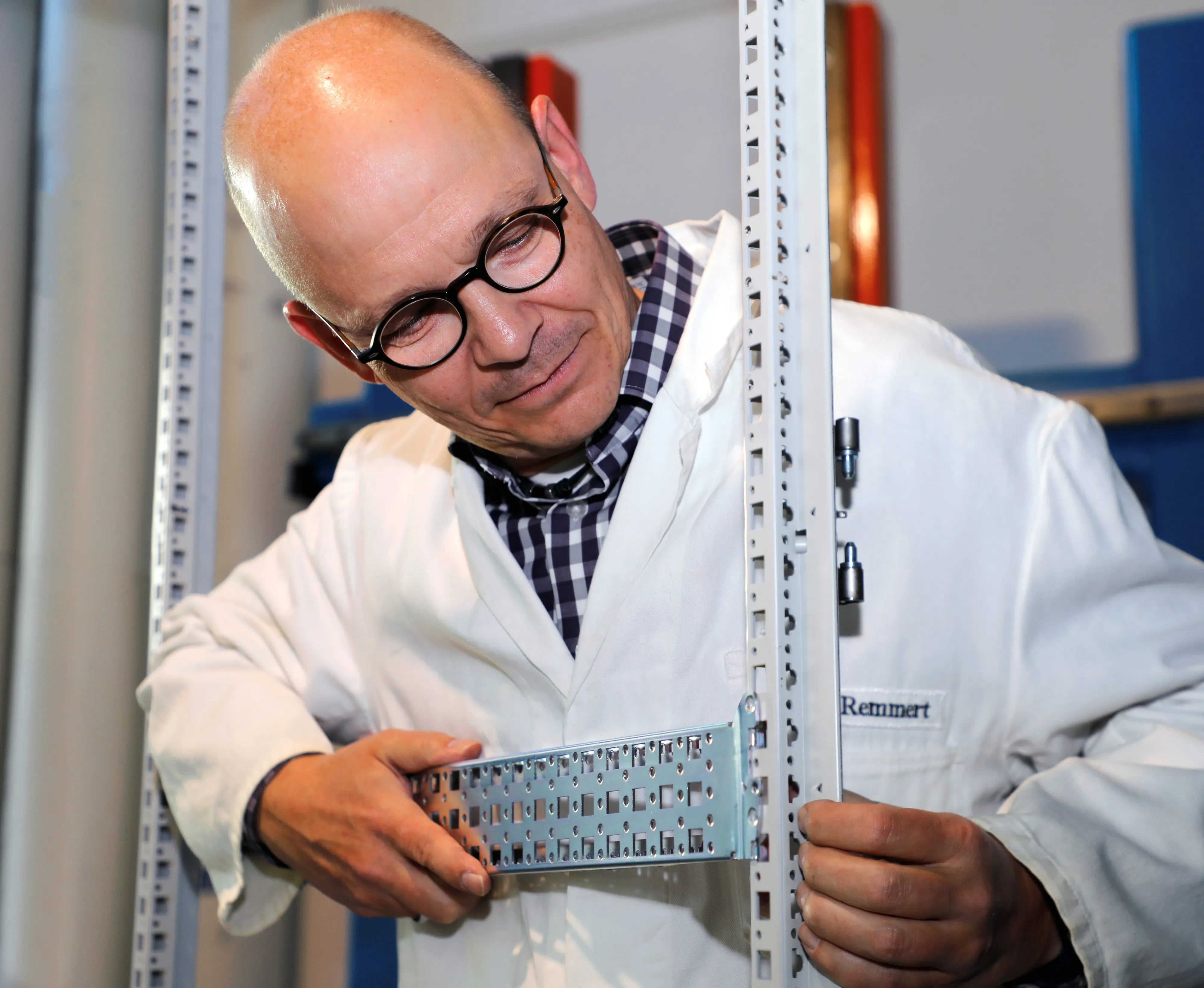 Ein Ingenieur von Rittal in einem Labor untersucht ein technisches Bauteil in einem Rahmengestell.
